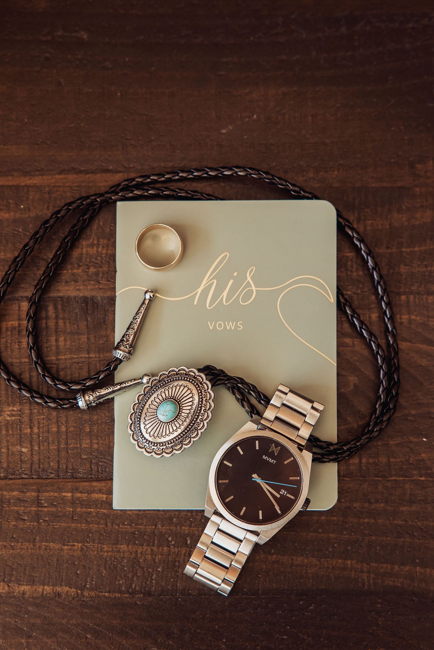 Wedding accessories including a brown leather watch and turquoise jewelry displayed on dark wood.