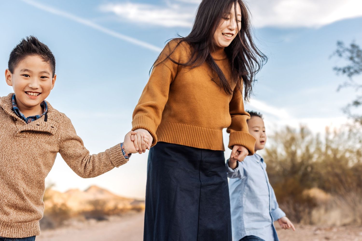 A happy family holds hands while walking along a desert trail during golden hour sunset.