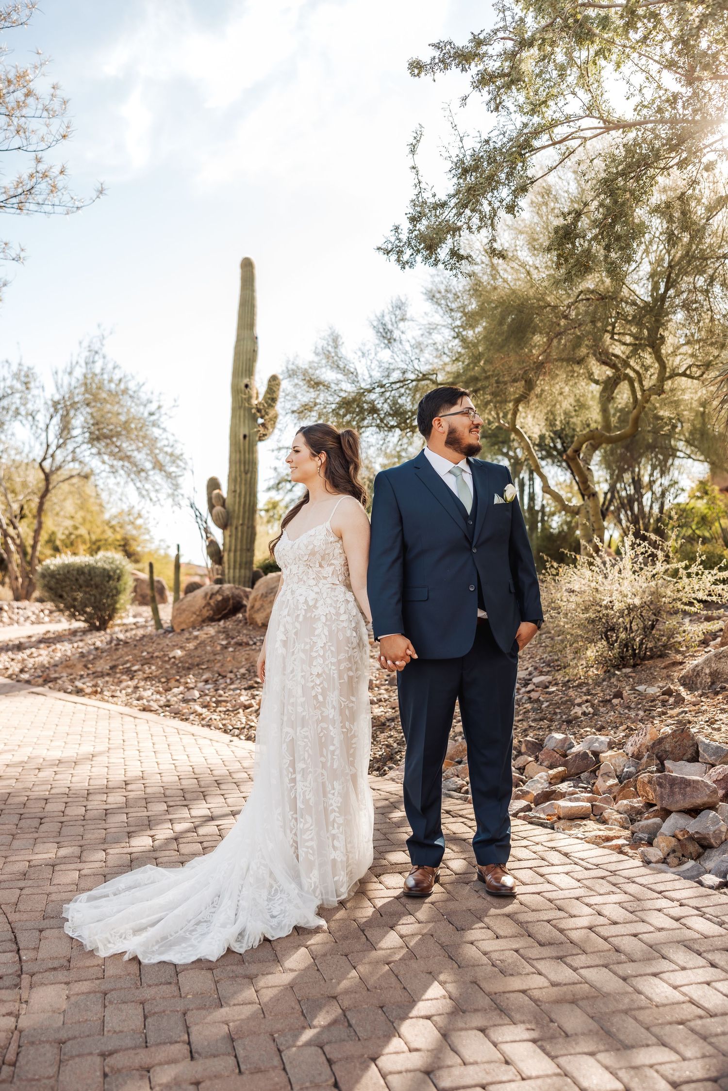 Wedding couple sharing intimate moments on a desert pathway lined with cacti and rocks.