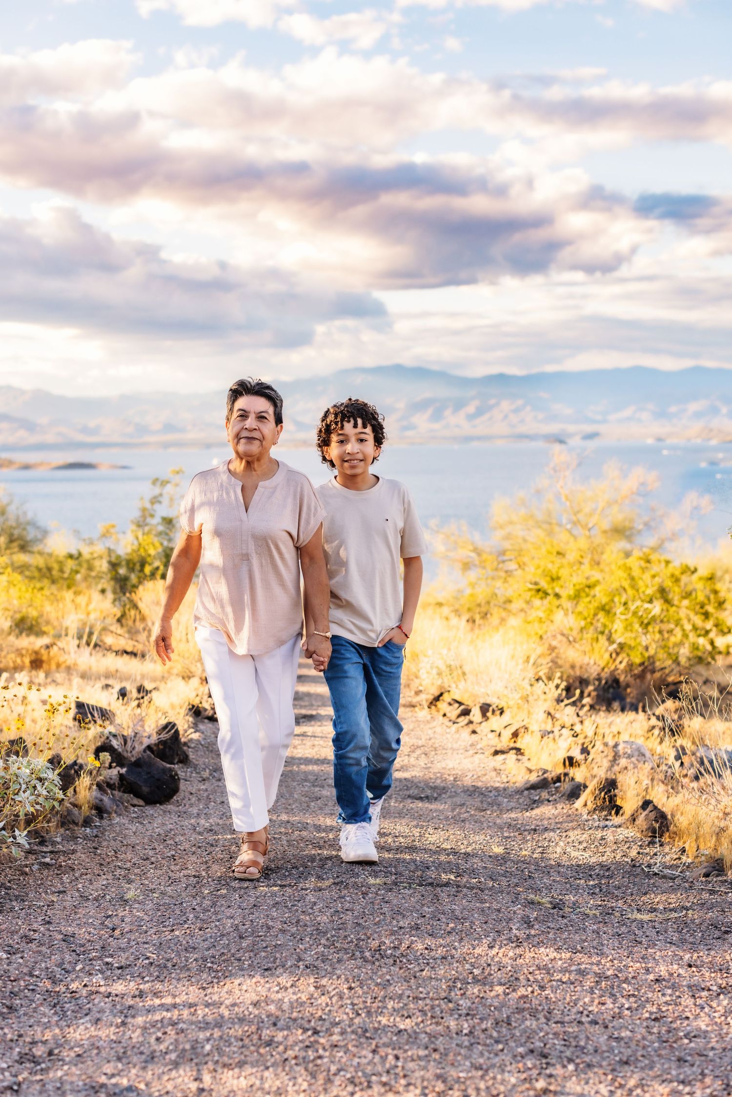 Two people walk a desert trail together at sunset with golden desert brush and mountains in the background.