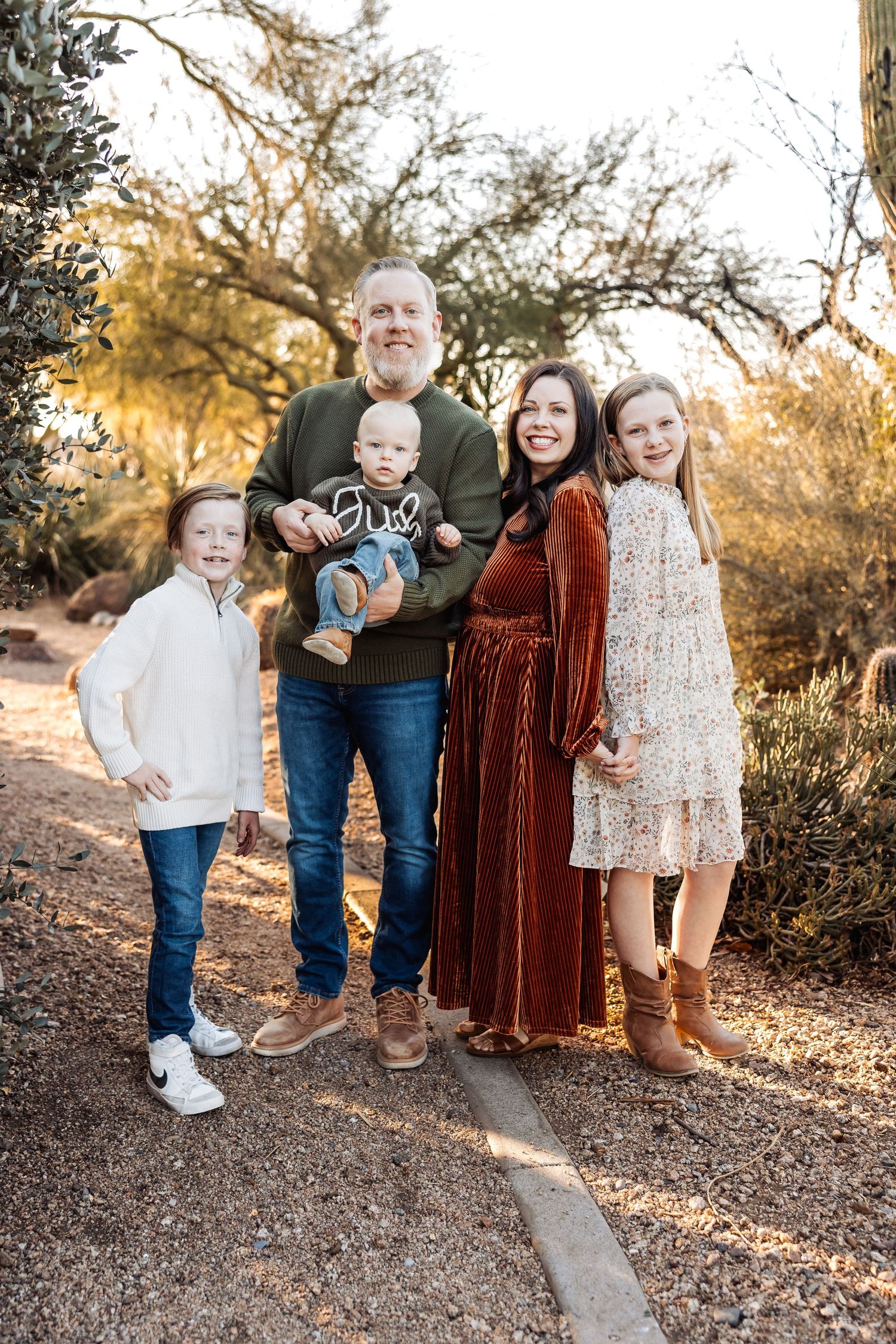 Family of five poses together on a desert hiking trail during golden hour wearing coordinated fall outfits.
