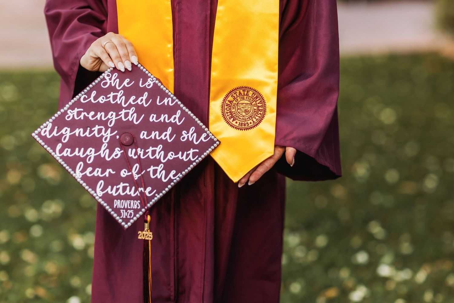 A decorative graduation cap with inspirational text alongside a yellow and burgundy graduation stole and gown.
