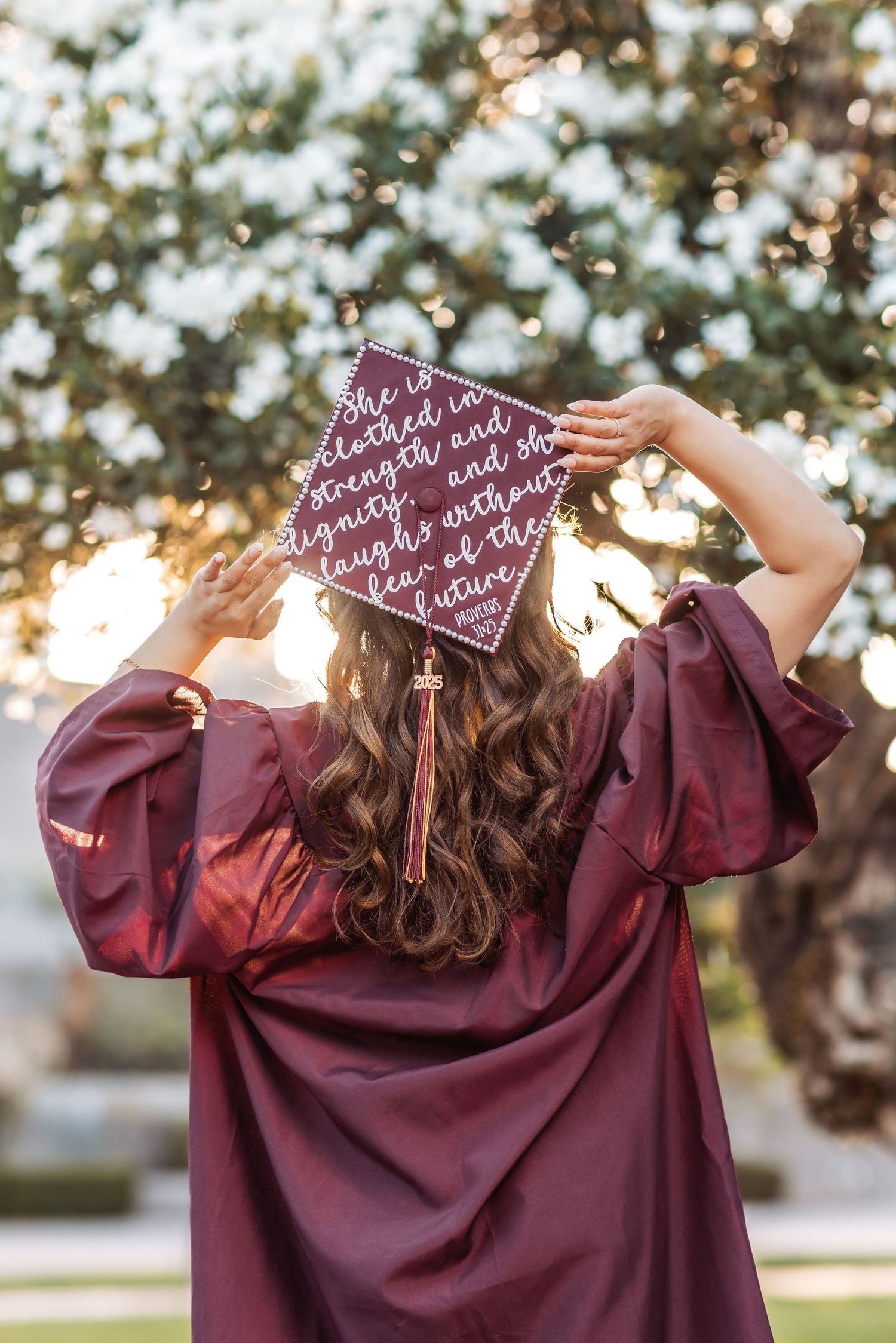Multiple views of a graduation cap decorated with burgundy writing displayed outdoors with trees in background.