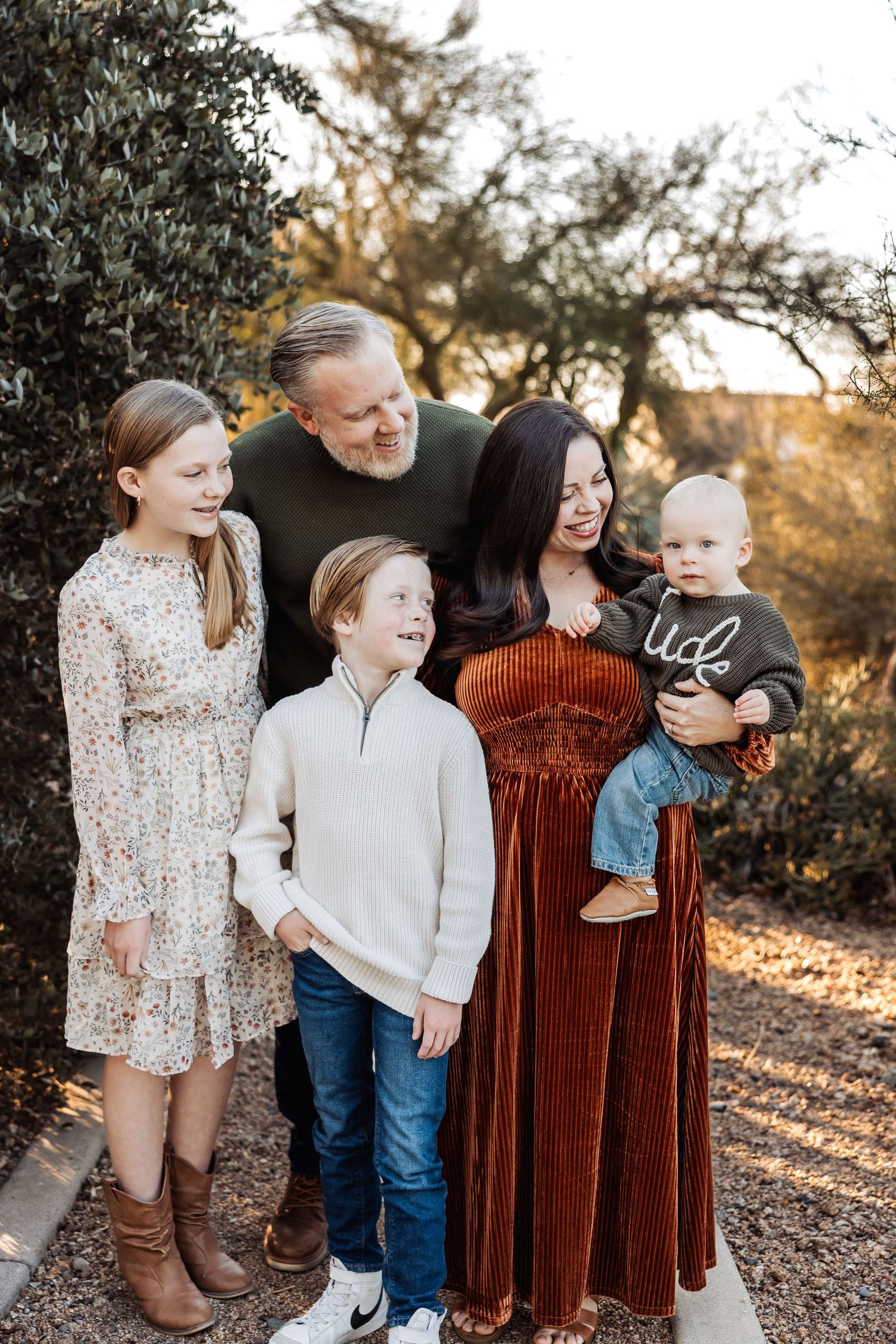 Family dressed in rustic boho clothing poses together on a scenic desert path at sunset.