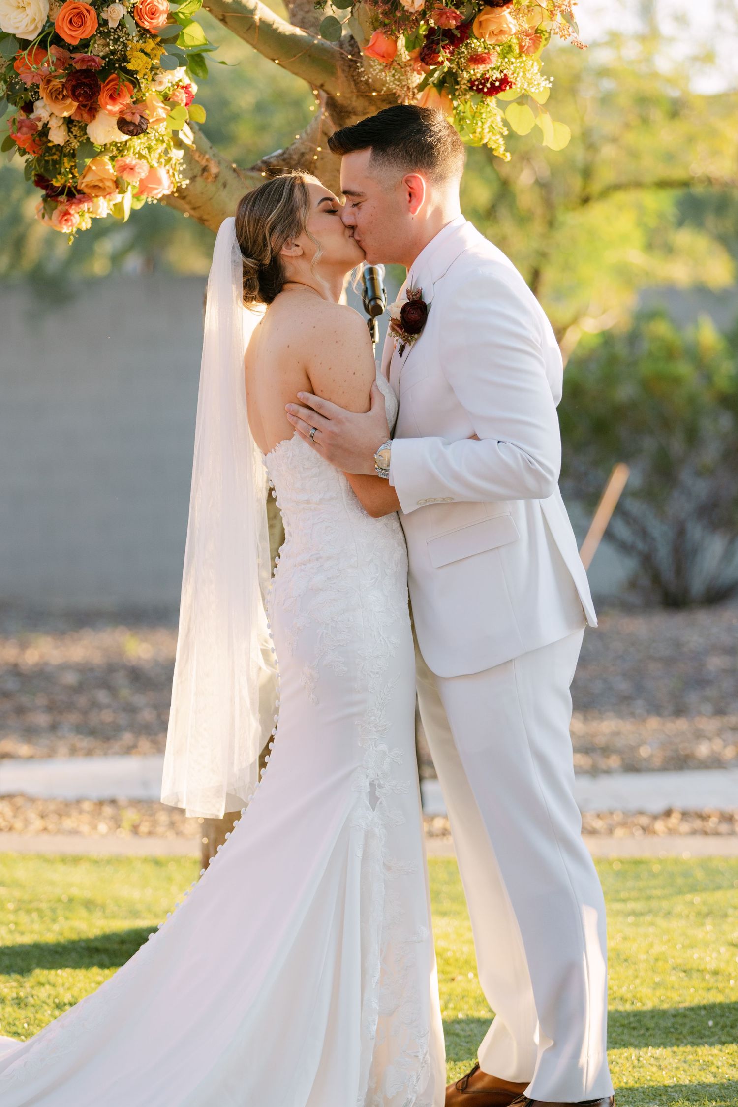 Romantic outdoor wedding ceremony moment under floral arch during sunset.