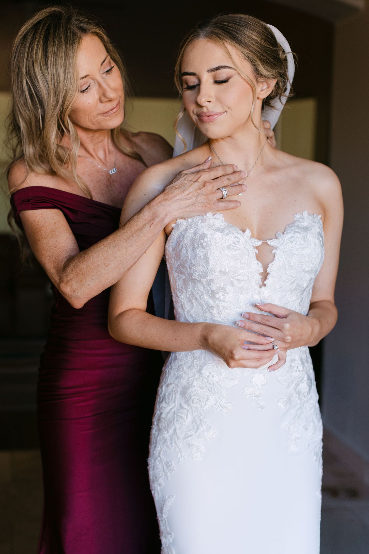 Two figures share an intimate moment in burgundy and white wedding attire during a pre-ceremony photoshoot.
