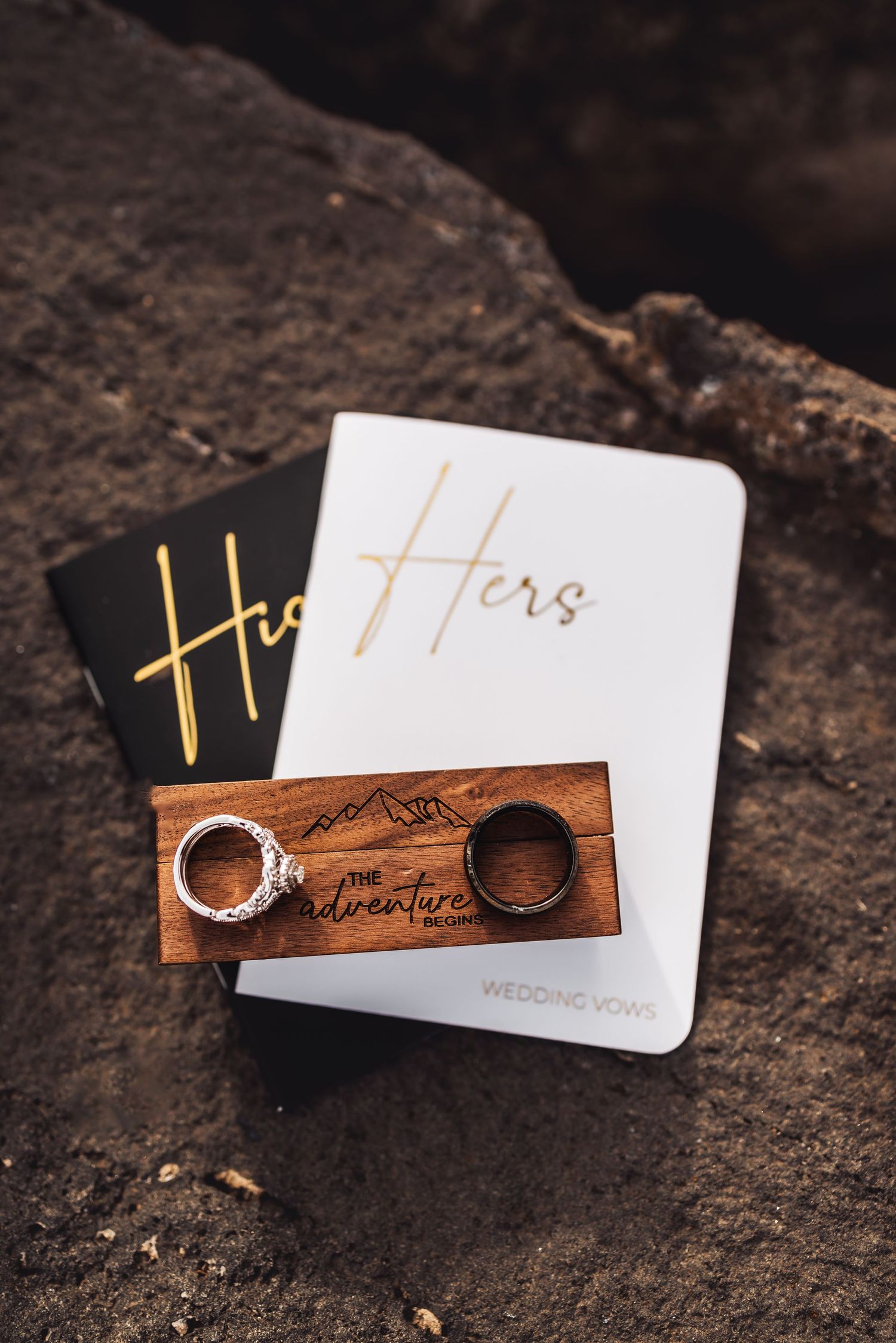 Wooden ring box with mountain engravings and wedding bands displayed on a dark textured surface.