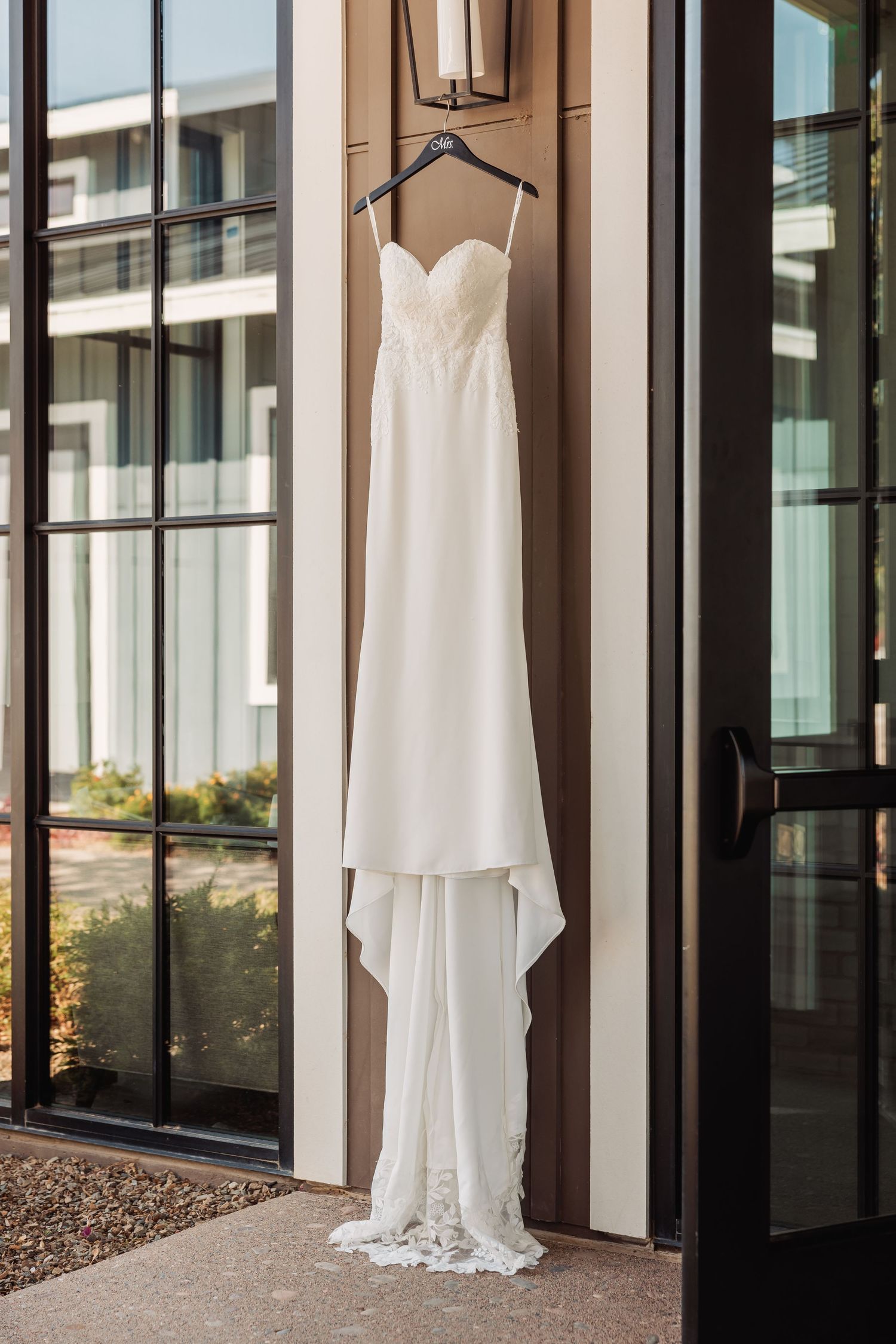 Elegant white wedding dresses hanging on display against modern glass windows in a bridal suite.