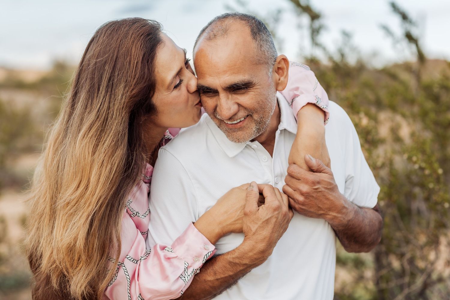 A loving couple embraces outdoors in a natural setting during a romantic photoshoot at sunset.
