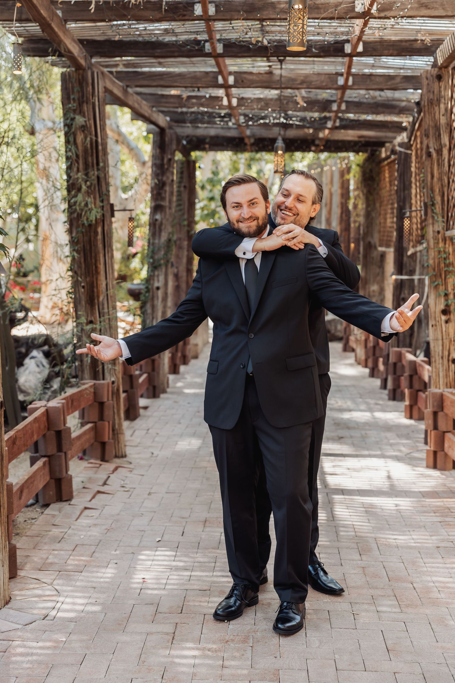 Groomsmen share playful moments in a rustic wooden pergola walkway during wedding photos.