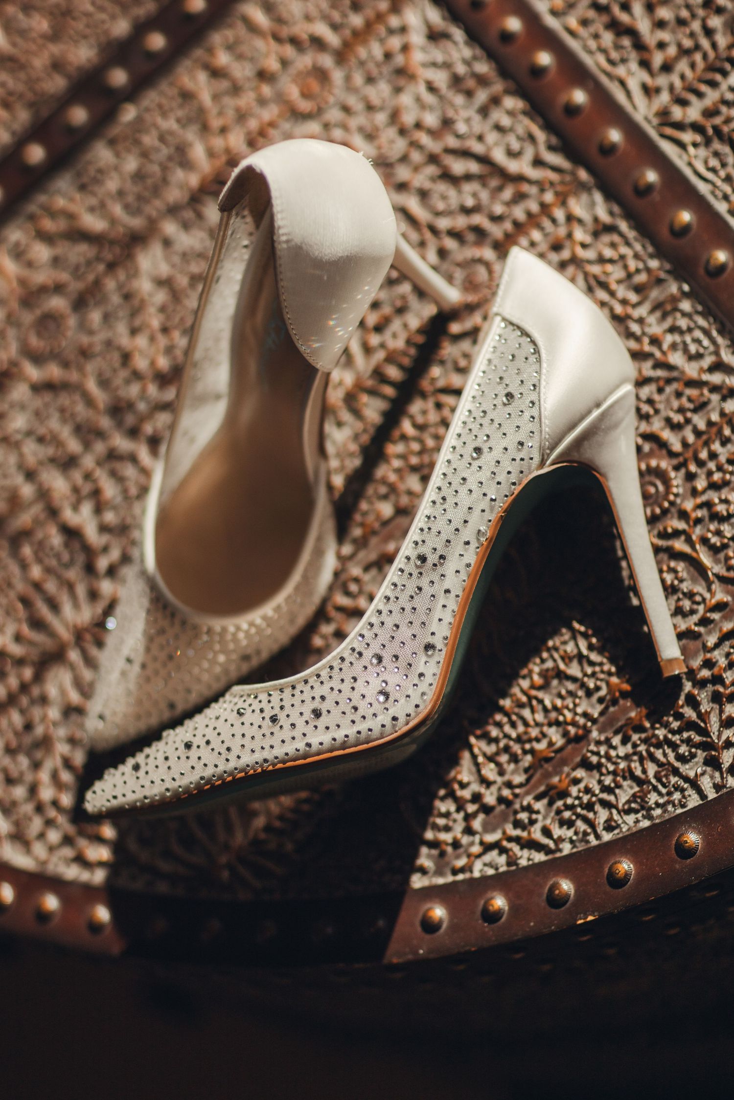 Close-up sequence of elegant white crystal-embellished high heel wedding shoes on textured metallic background.