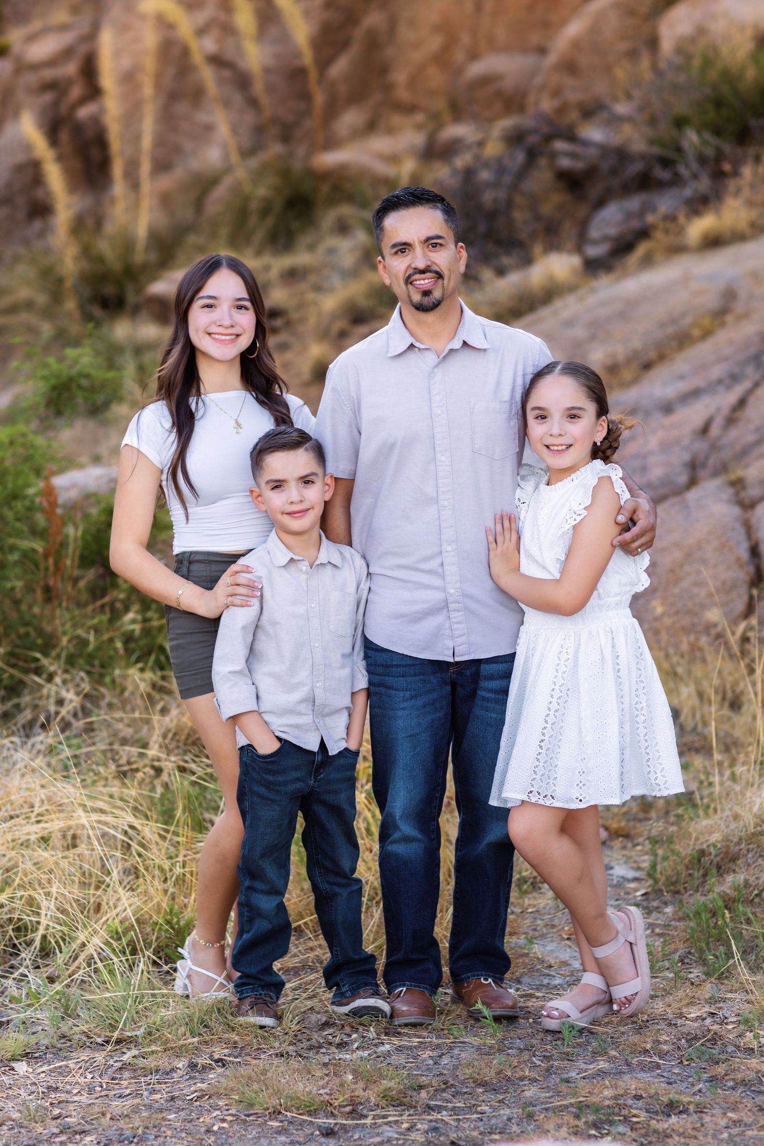A family wearing coordinated white and blue outfits poses together against a rocky outdoor backdrop.