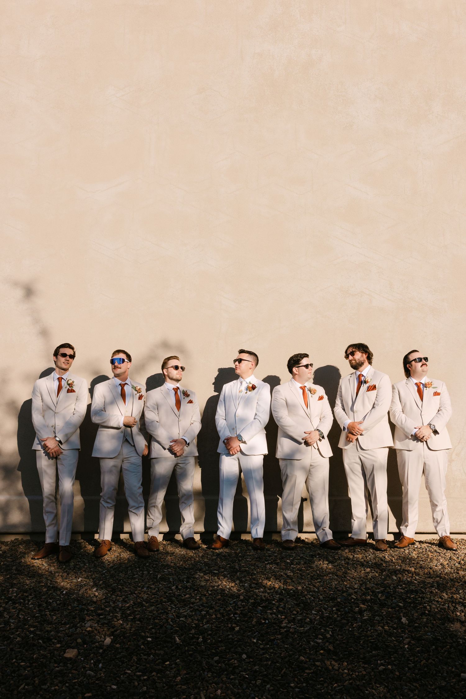 A wedding party in light gray suits and sunglasses poses in a line against a dark background.