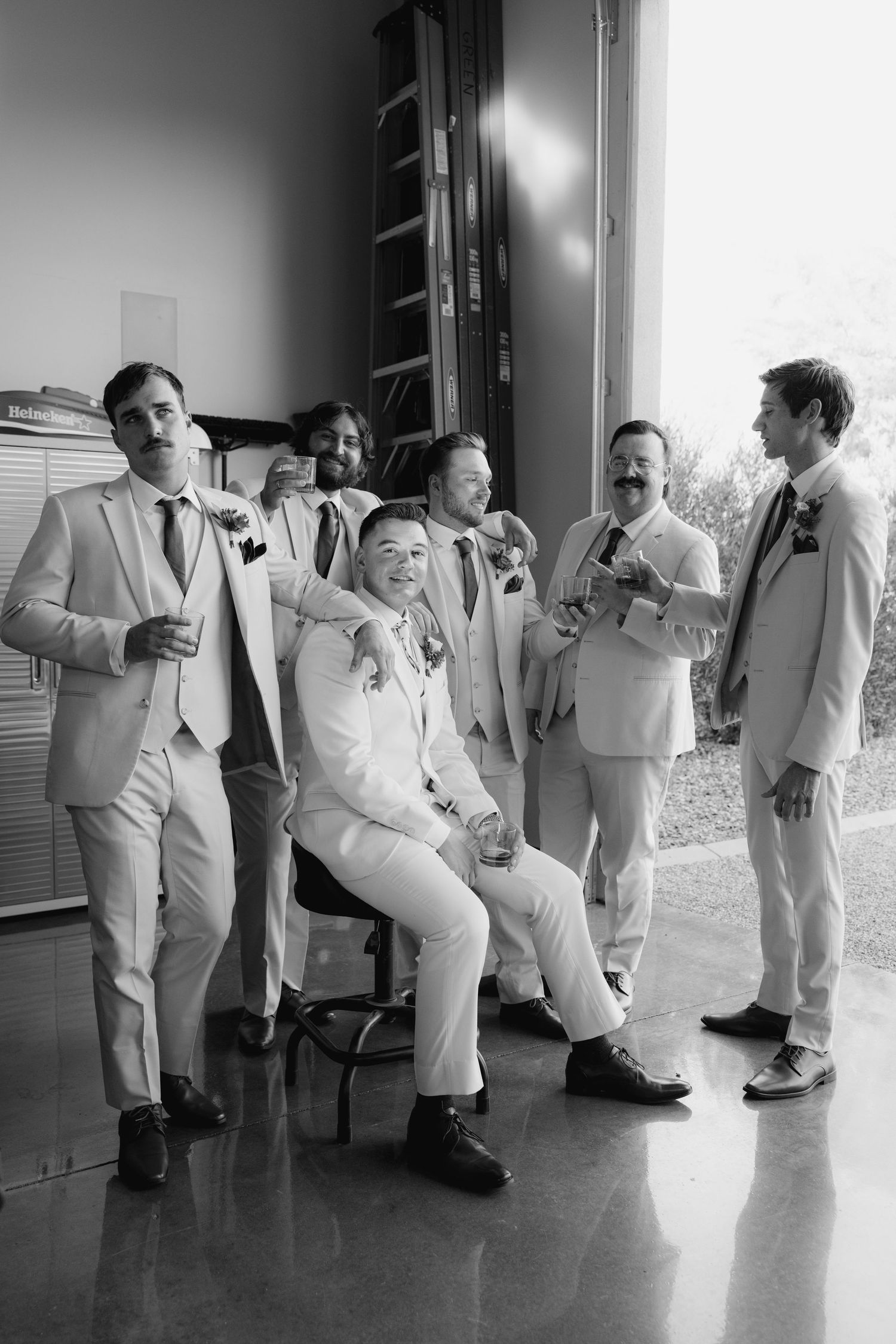 A sequence of black and white photos showing groomsmen in white suits performing playful dance moves in a hallway.