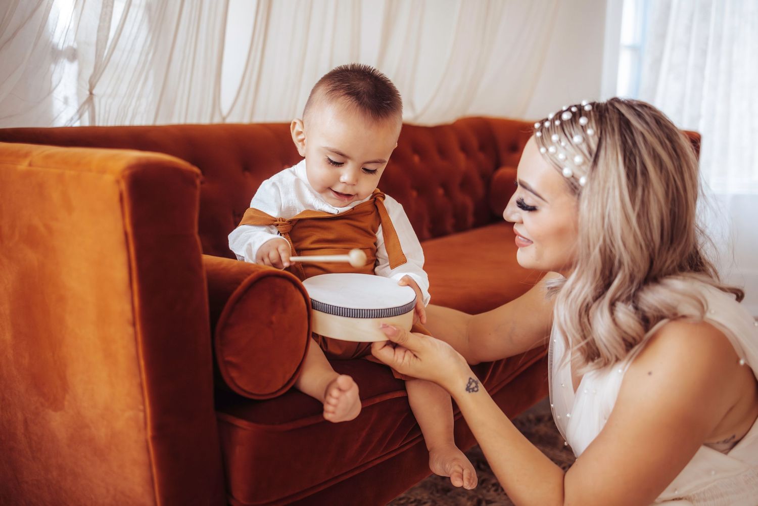 Intimate moment shared on an orange velvet couch as parent helps child with a cup of milk.