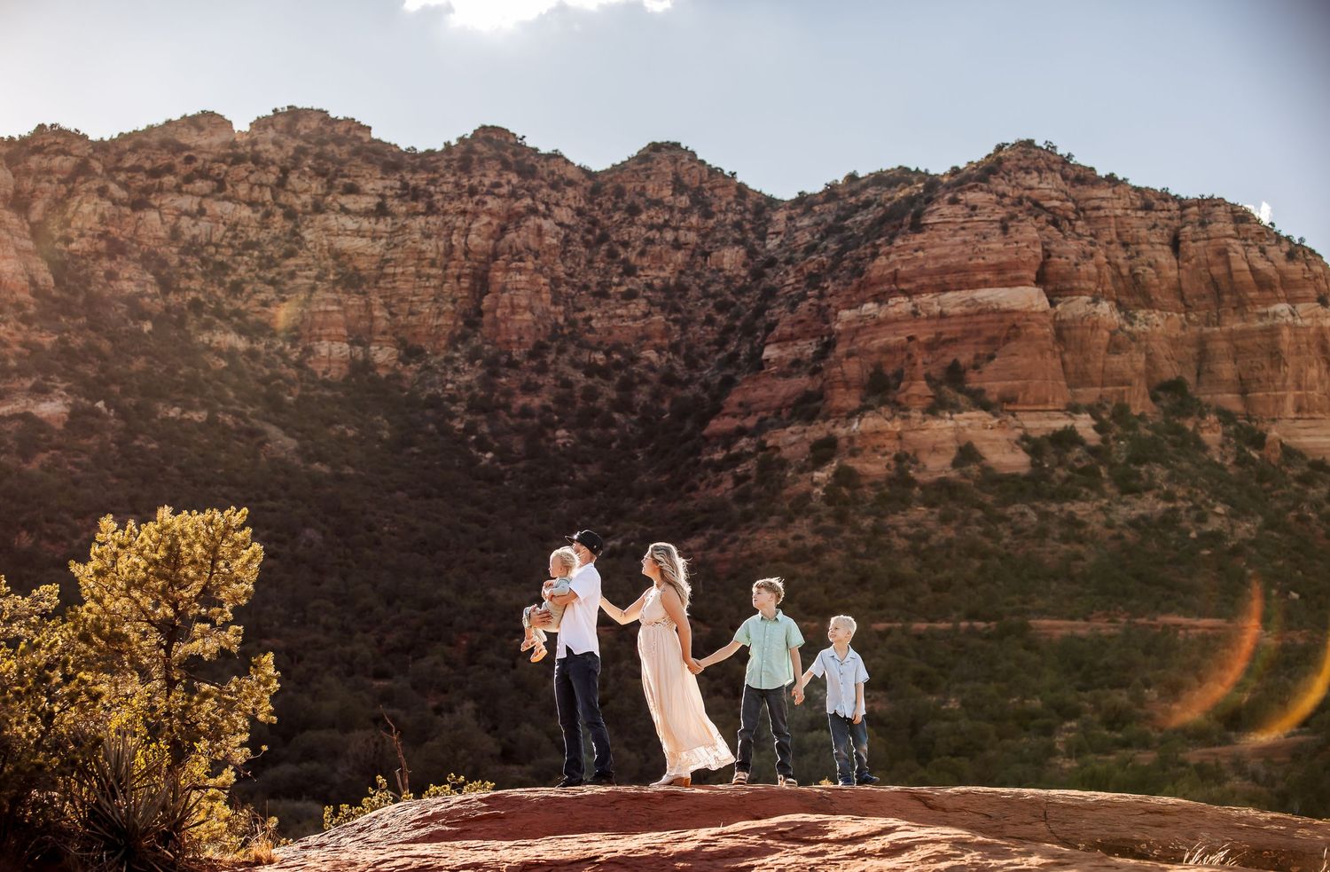A panoramic view of red rock formations at sunset in Sedona, Arizona with desert landscape and mountains in background.