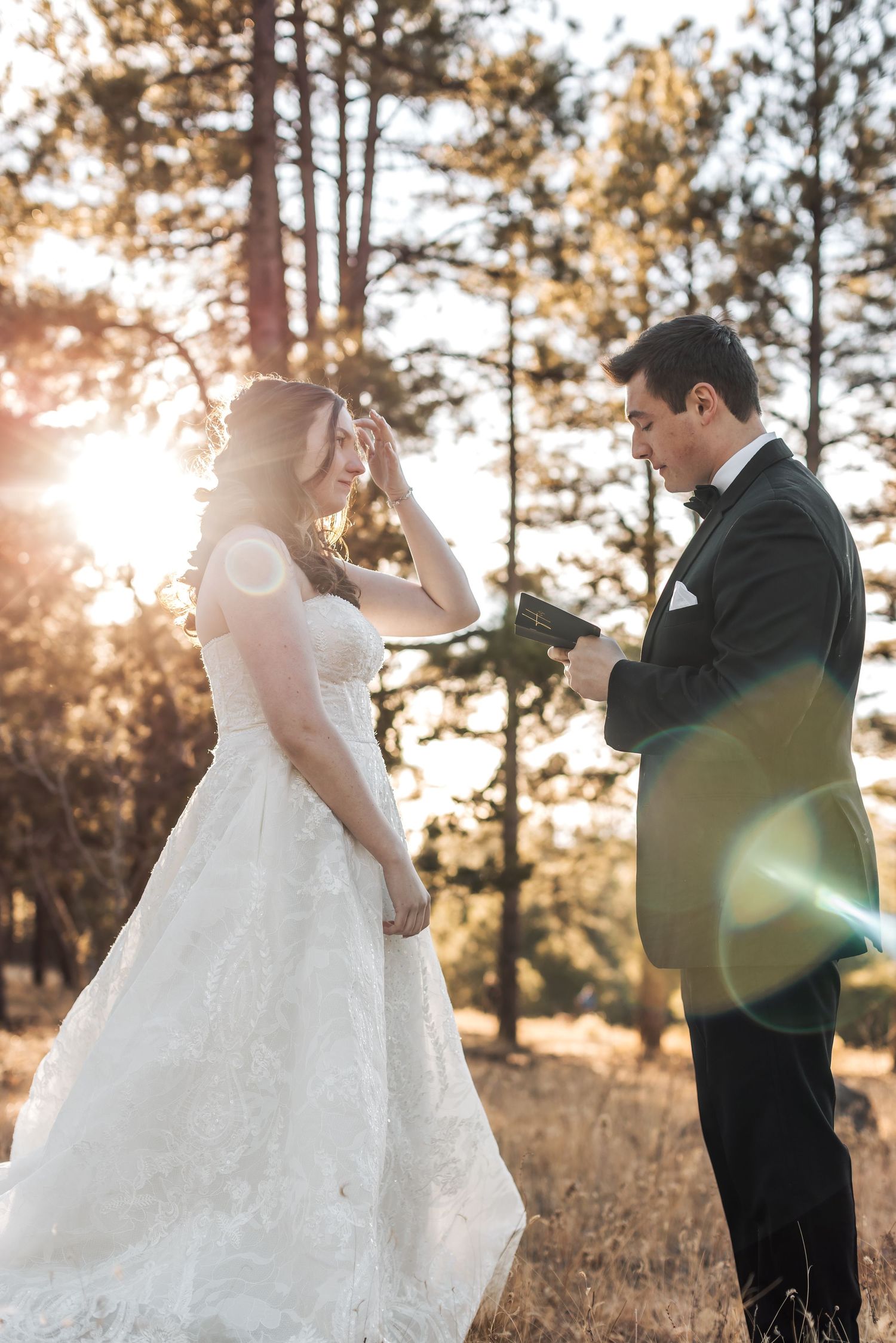 A couple in wedding attire shares intimate moments in a sunlit pine forest during golden hour.