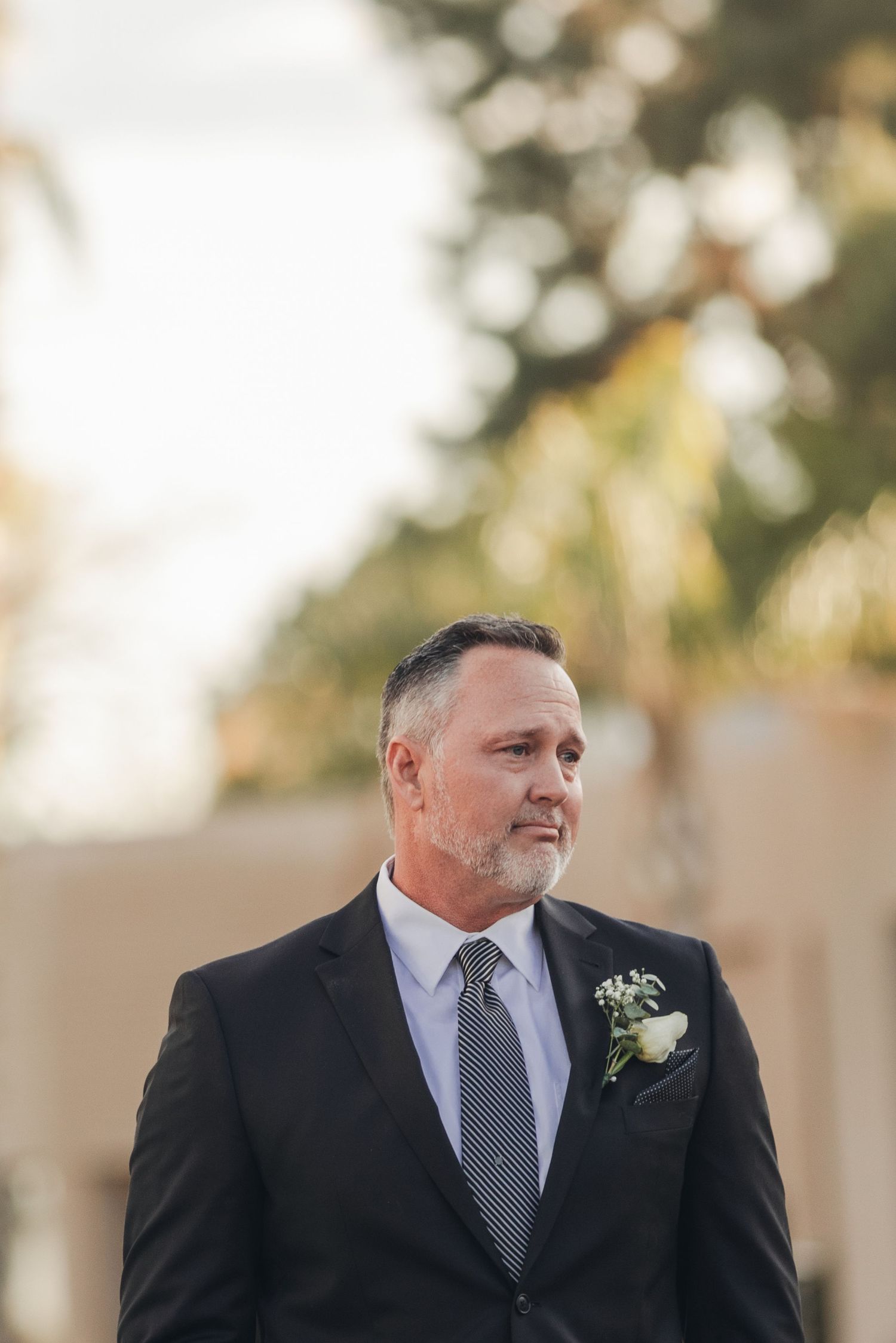 A person wearing a dark suit and tie with a boutonniere looks off to the side during a formal event.
