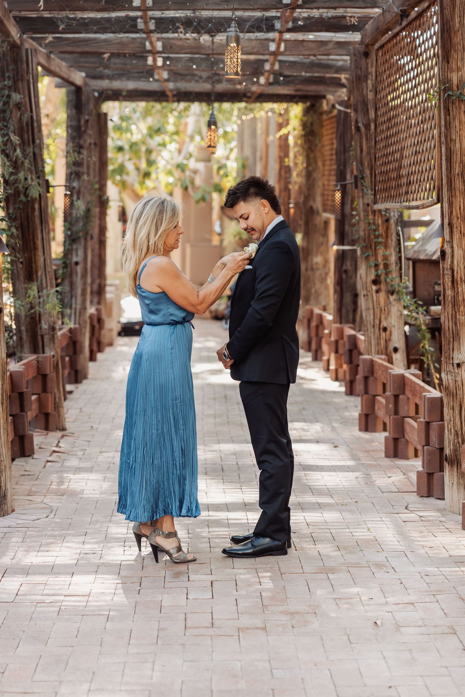 Couple in formal attire sharing a moment under a rustic wooden pergola walkway.