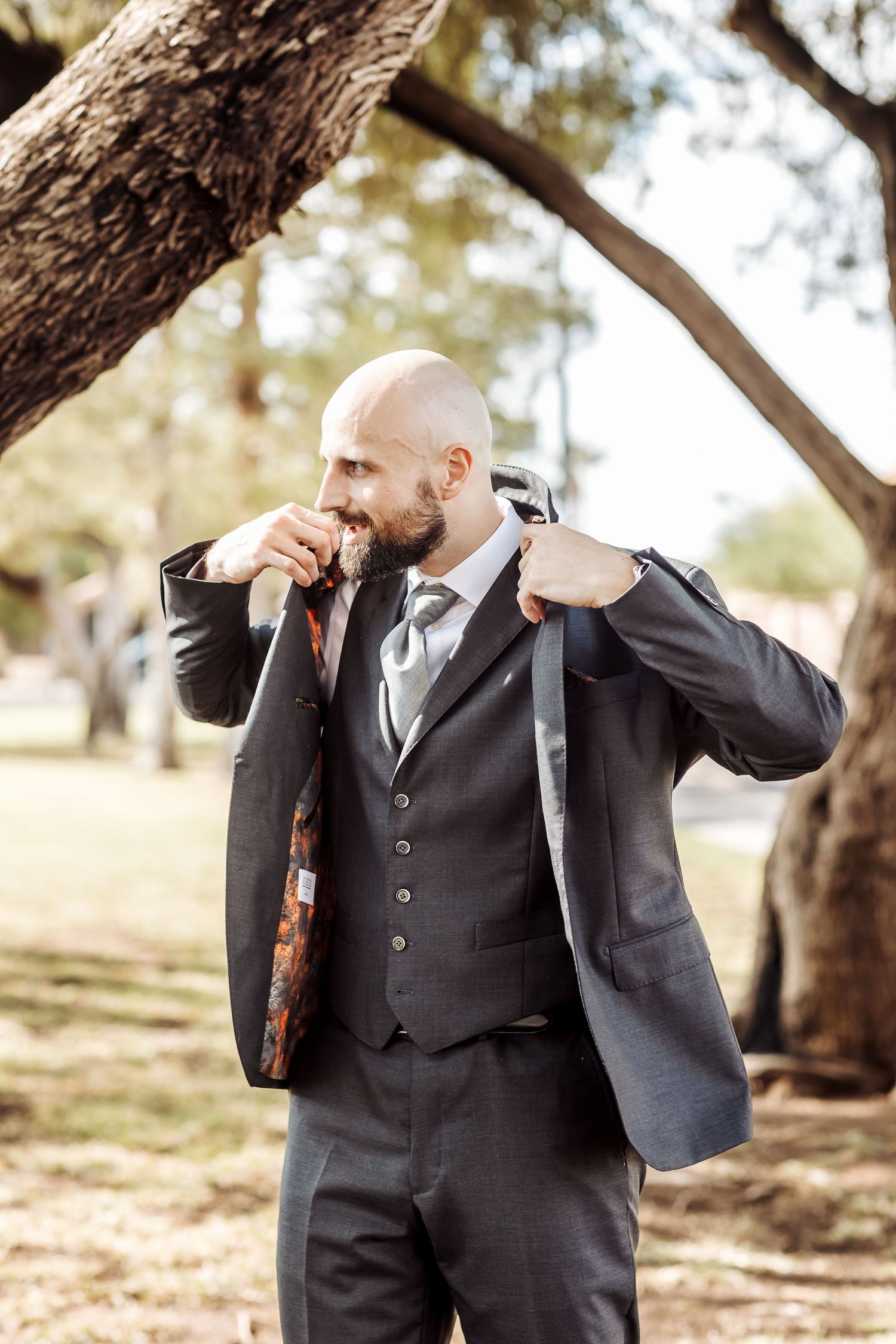A sequence of shots showing a groom in a dark suit and vest adjusting his tie outdoors under trees.