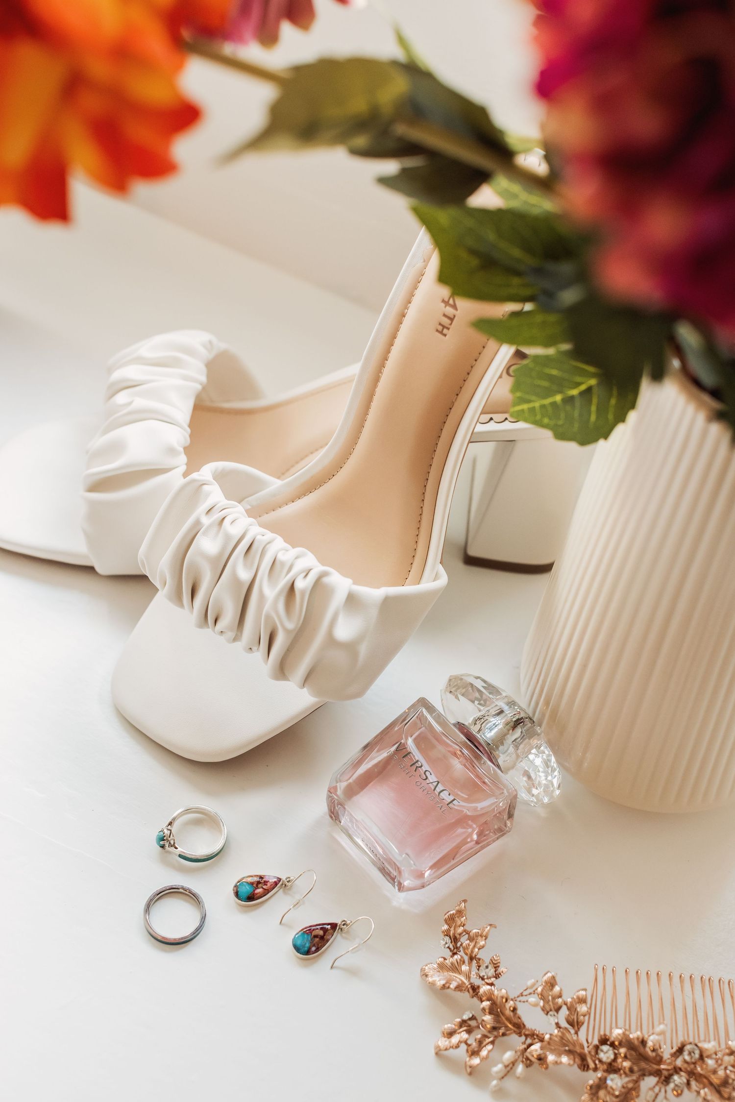 Wedding accessories including white shoes, rings, and perfume arranged with floral elements.
