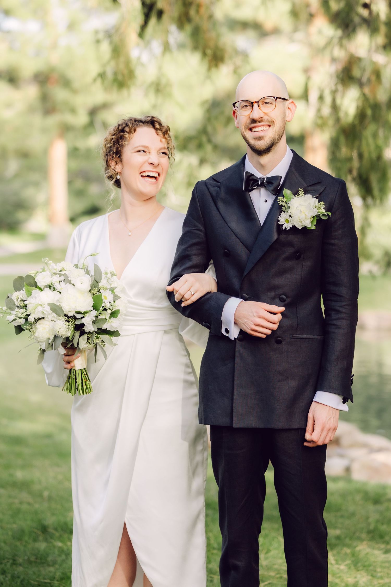 Newlywed couple shares joyful candid moments in outdoor wedding photos with white floral bouquet and classic attire.