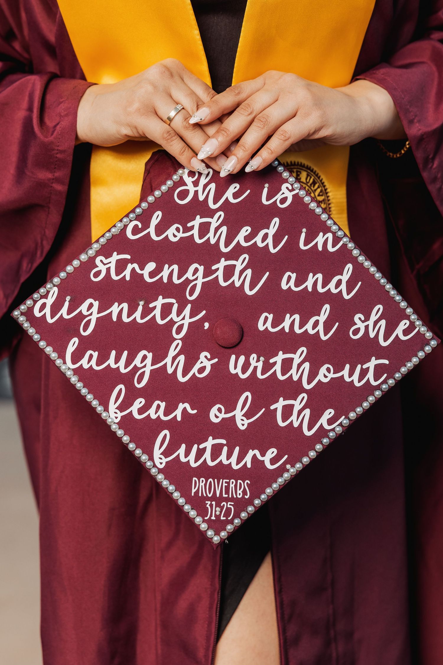 Decorated graduation cap with inspirational quote from Proverbs 31:25 on maroon and gold background.