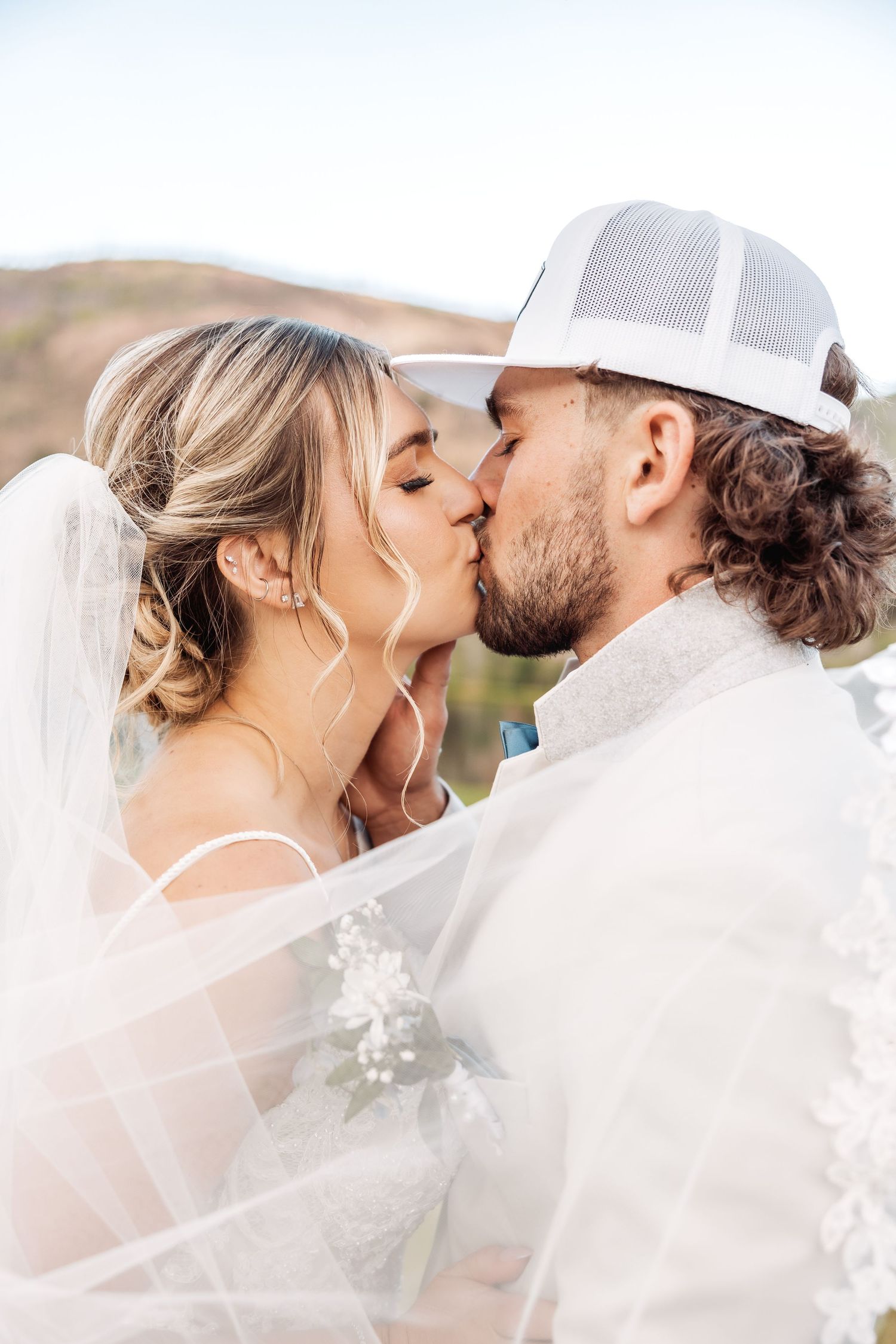A romantic wedding couple sharing intimate kisses under a flowing white veil.