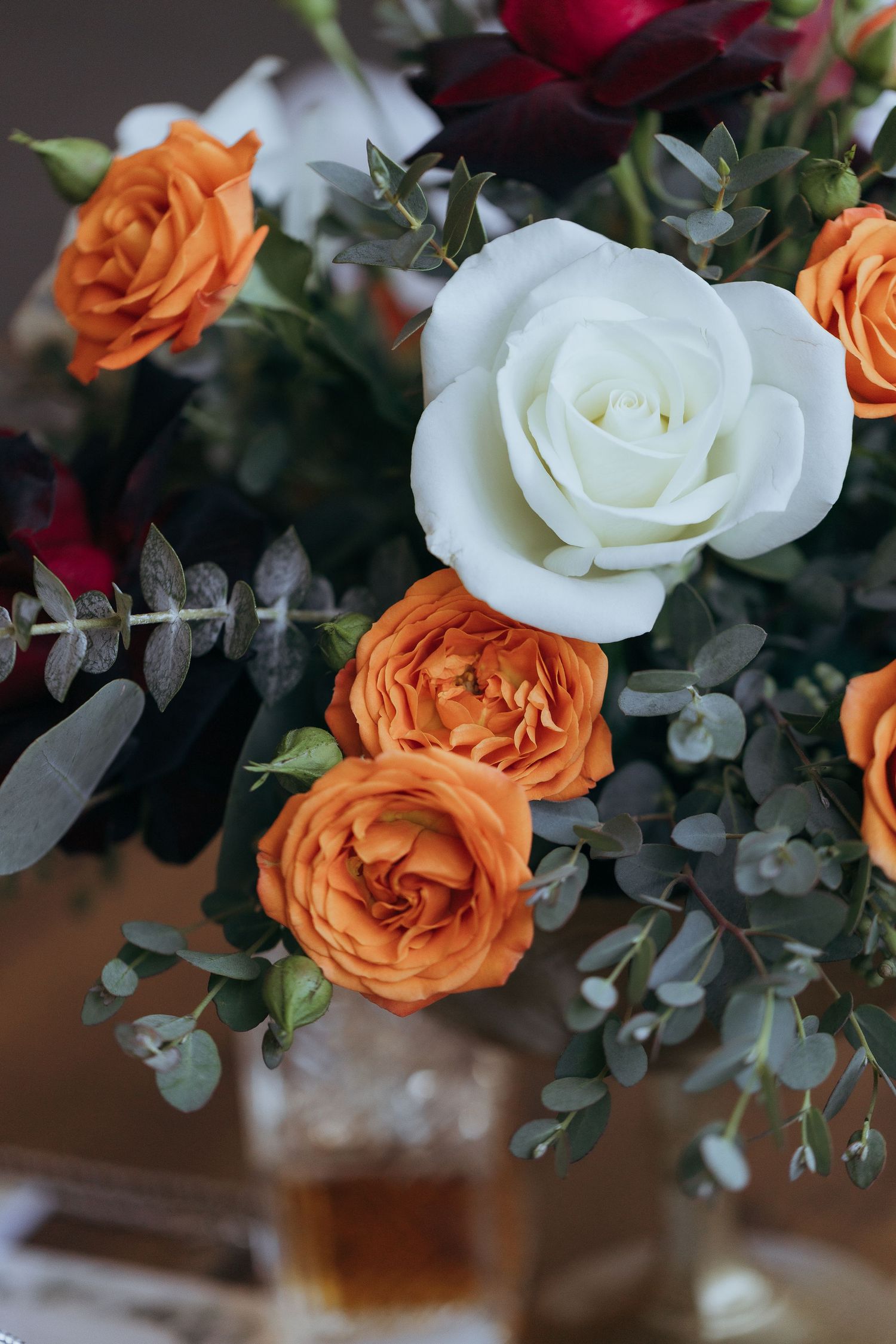 A beautiful floral arrangement featuring white and orange roses with eucalyptus leaves in soft natural lighting.