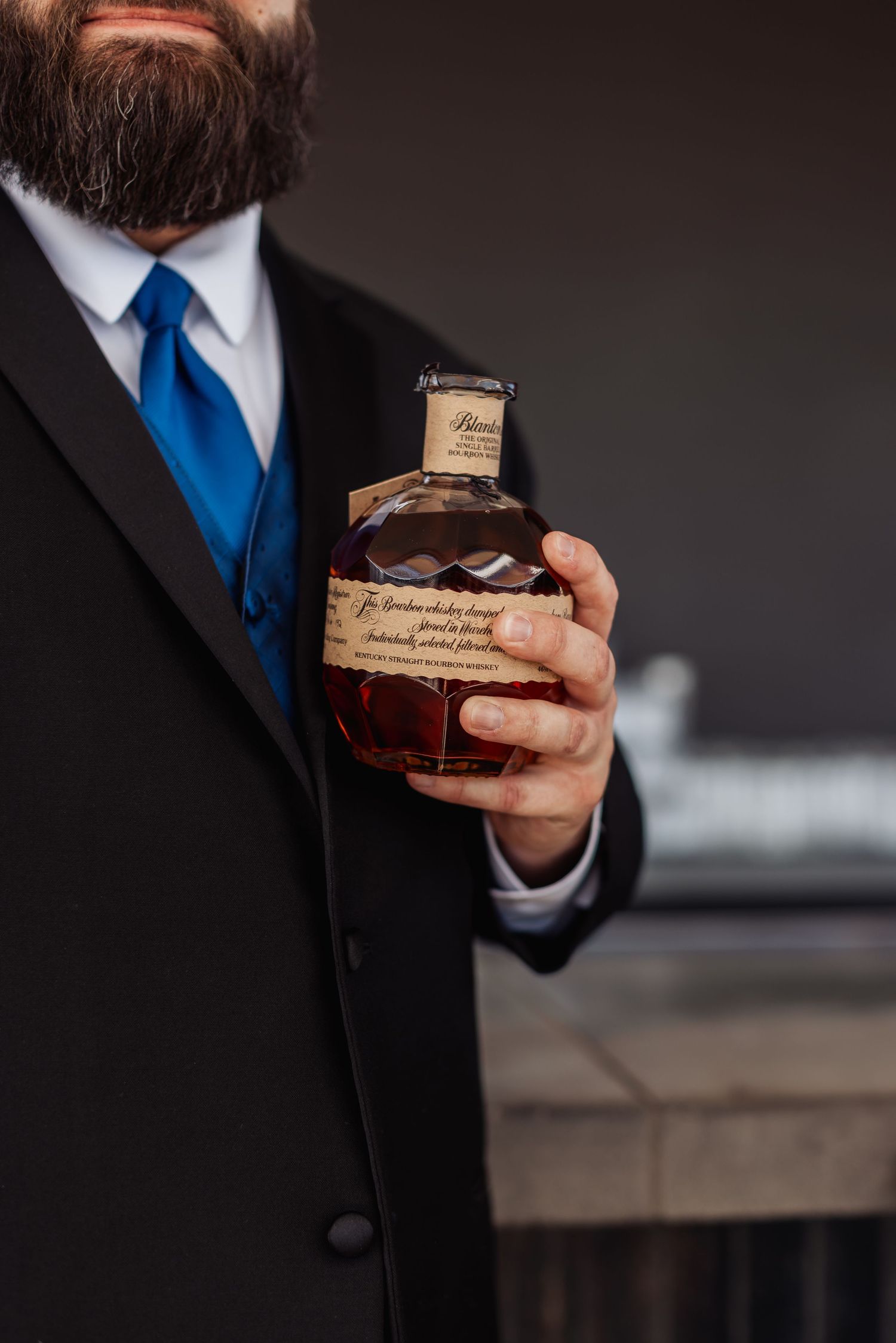Person in black suit holding a small wooden box against dark background.