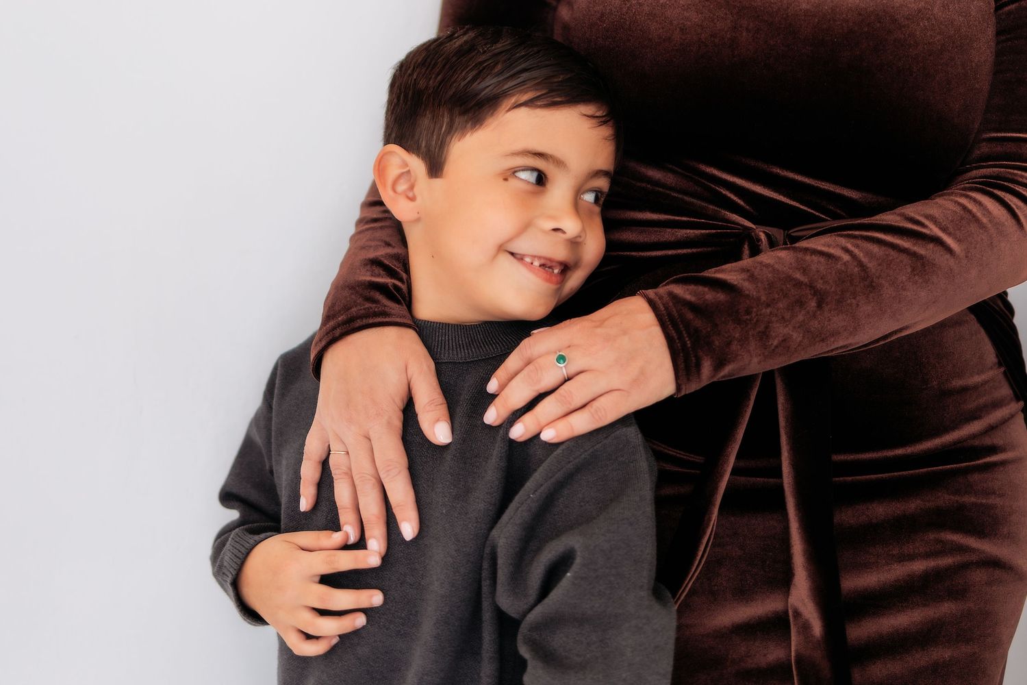 A person in a gray sweater stands next to someone wearing brown while sharing a warm embrace.