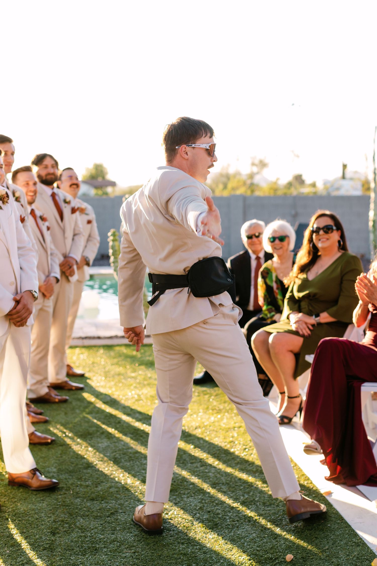 Wedding guests in formal attire performing synchronized dance moves outdoors.