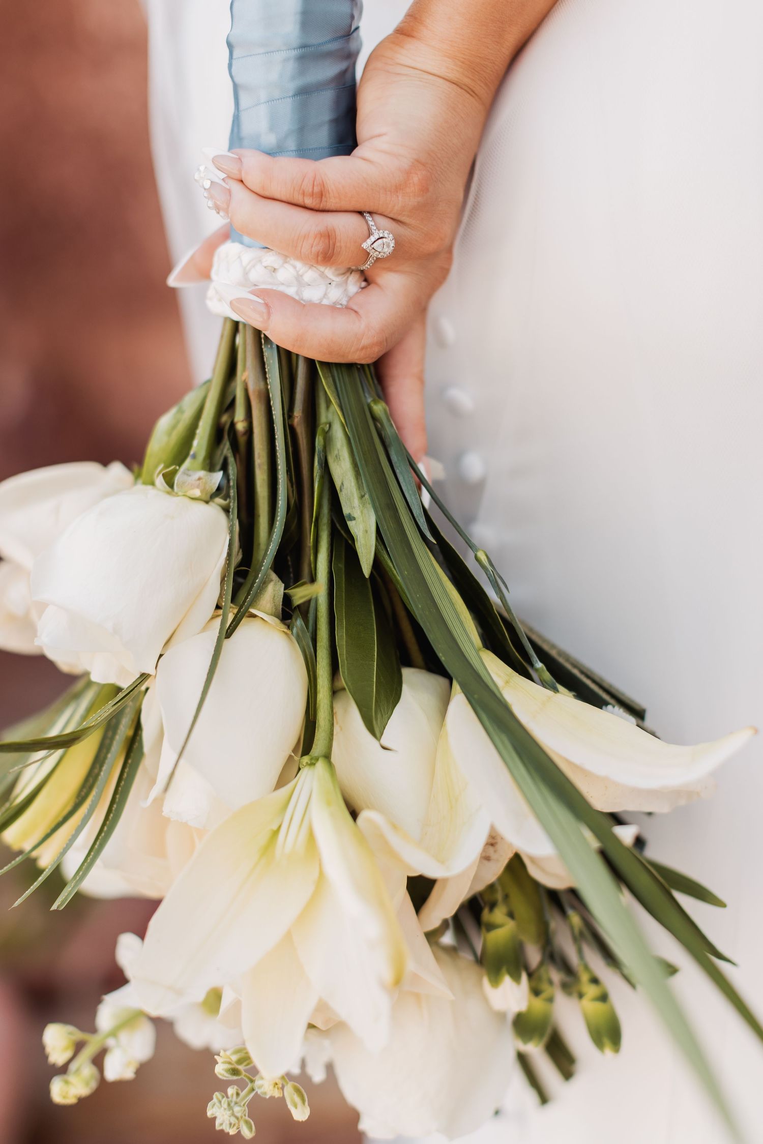 Close-up of hands holding a white floral wedding bouquet, showcasing engagement ring details.