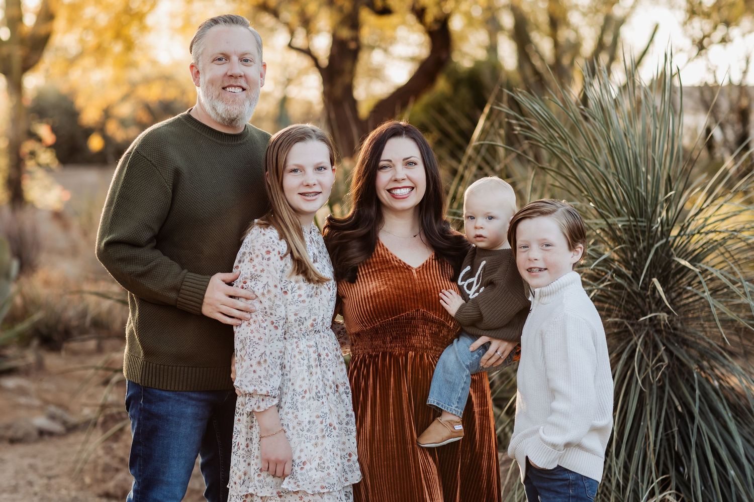 Family wearing earth-toned clothing poses together among desert plants at golden hour.
