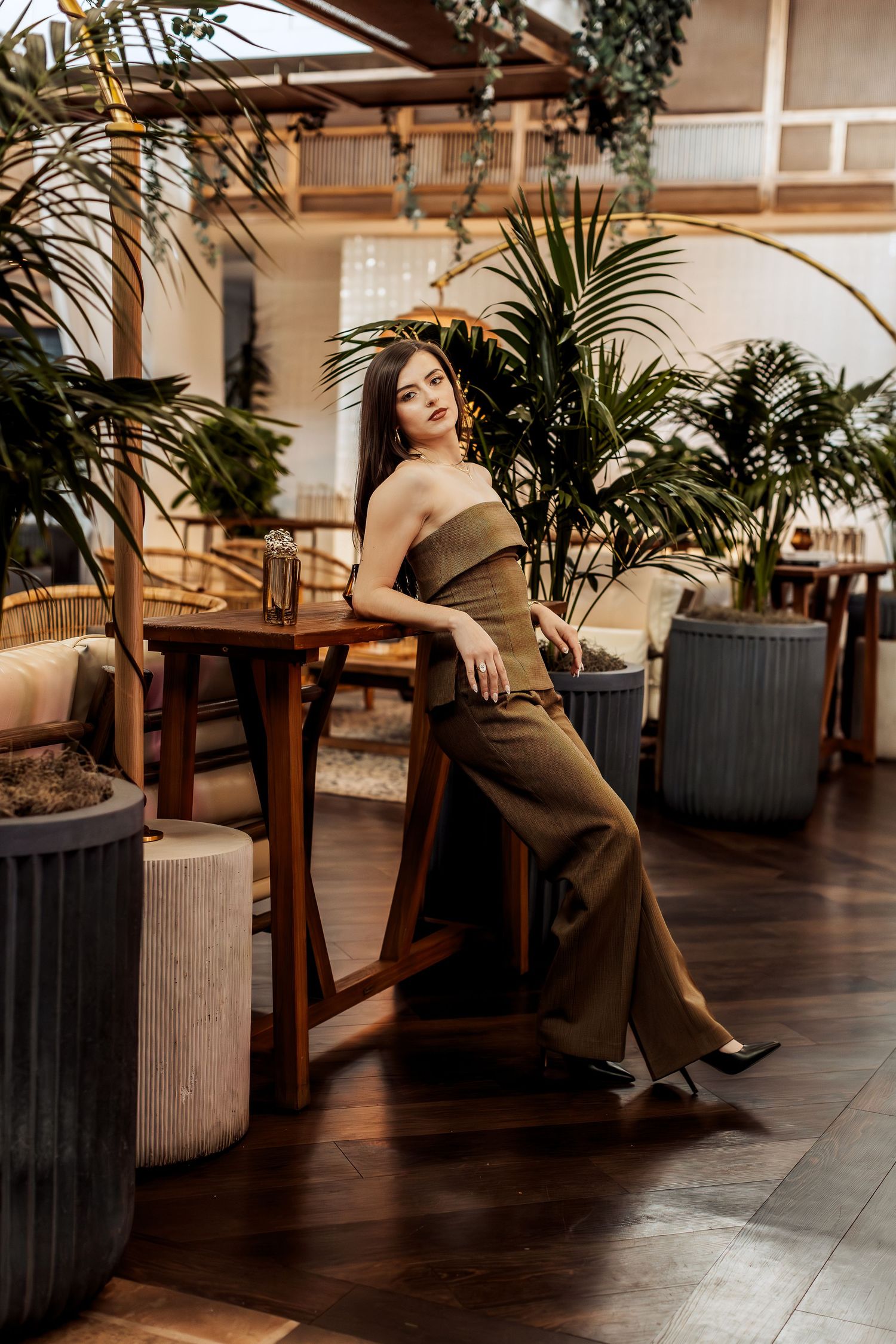Fashion photoshoot in an elegant indoor space with tropical plants and wooden furniture against dark flooring.