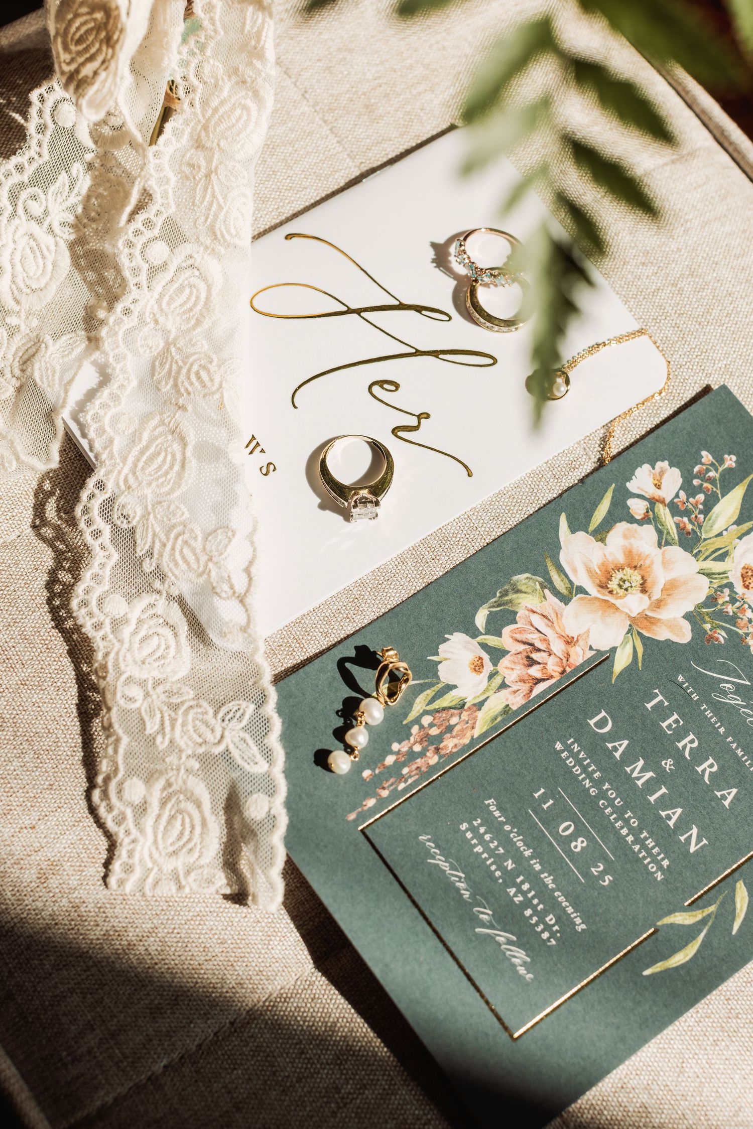 Elegant sage green and white wedding invitations with floral details and wedding rings in natural light.