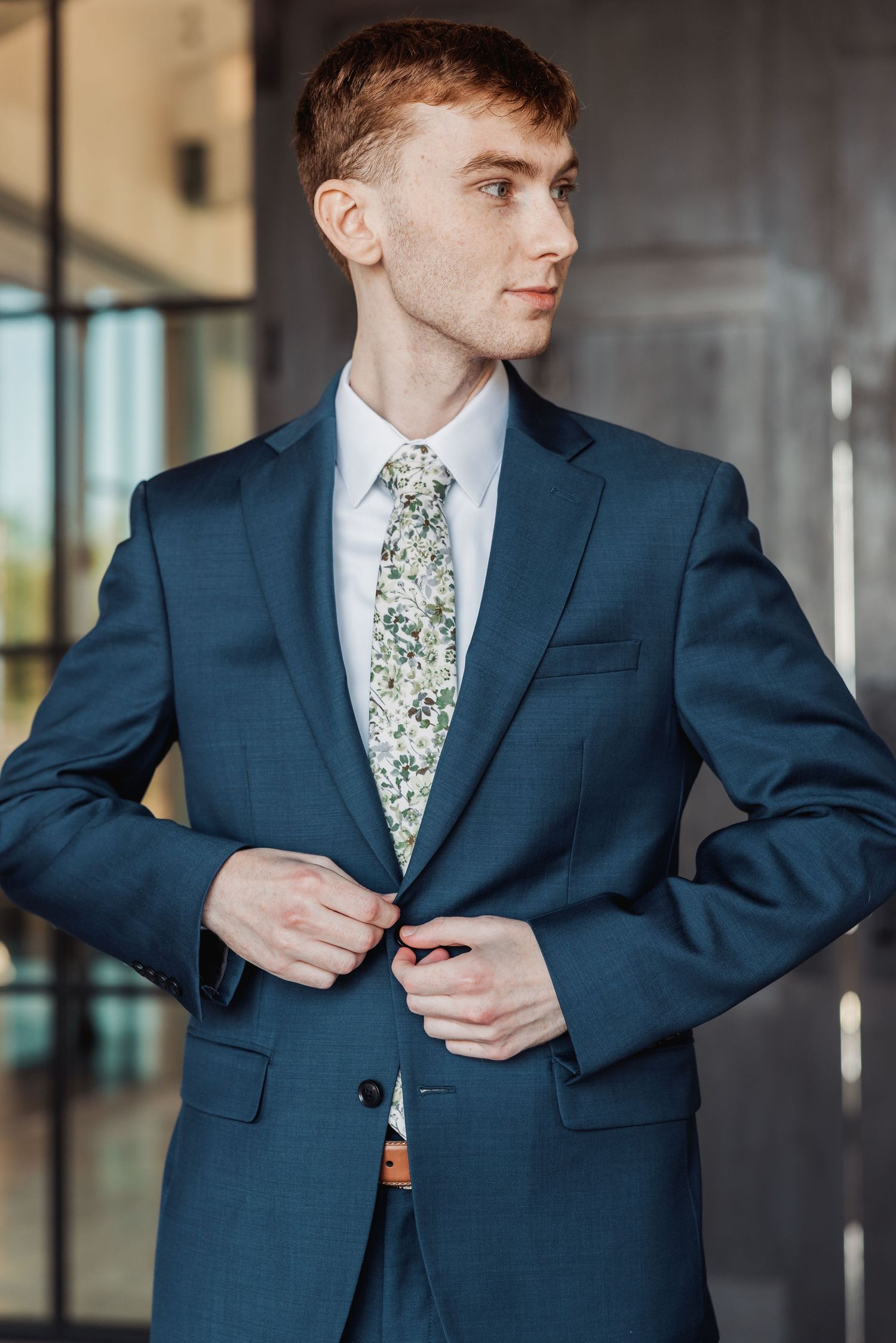 Close-up shots of a navy blue suit jacket with floral tie being buttoned in an elegant setting.