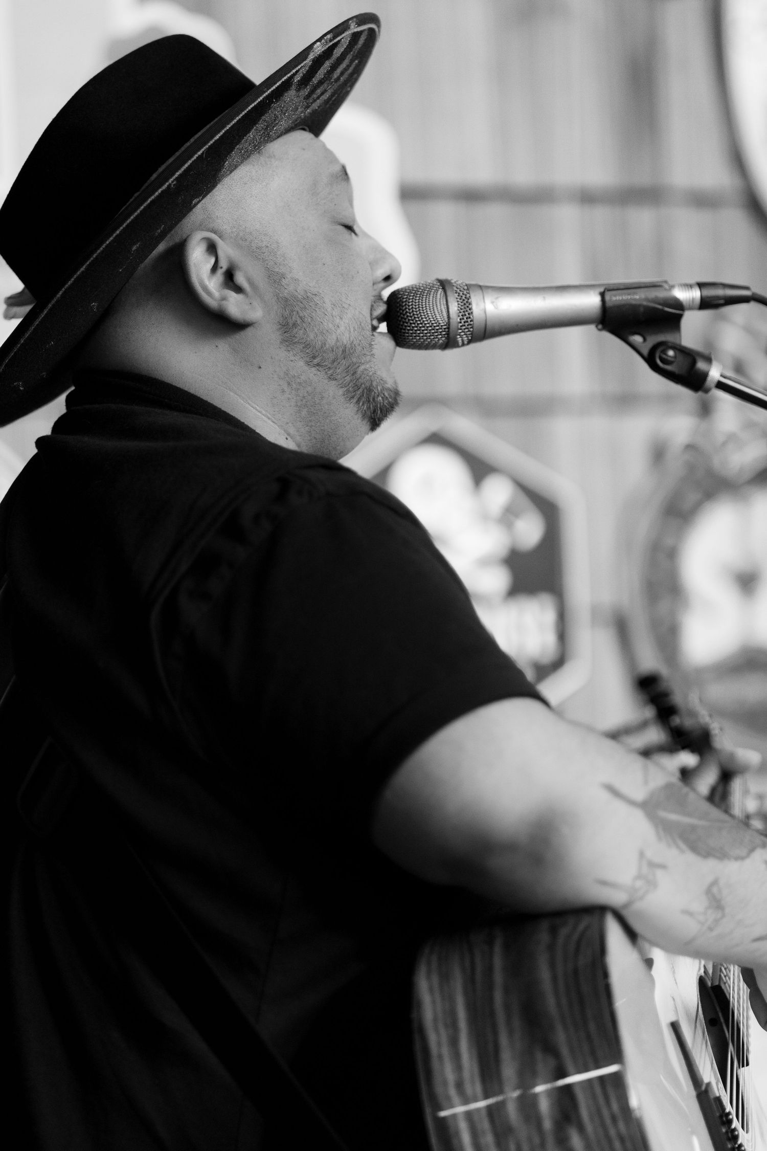 A performer in a black hat sings into a microphone during a live performance.