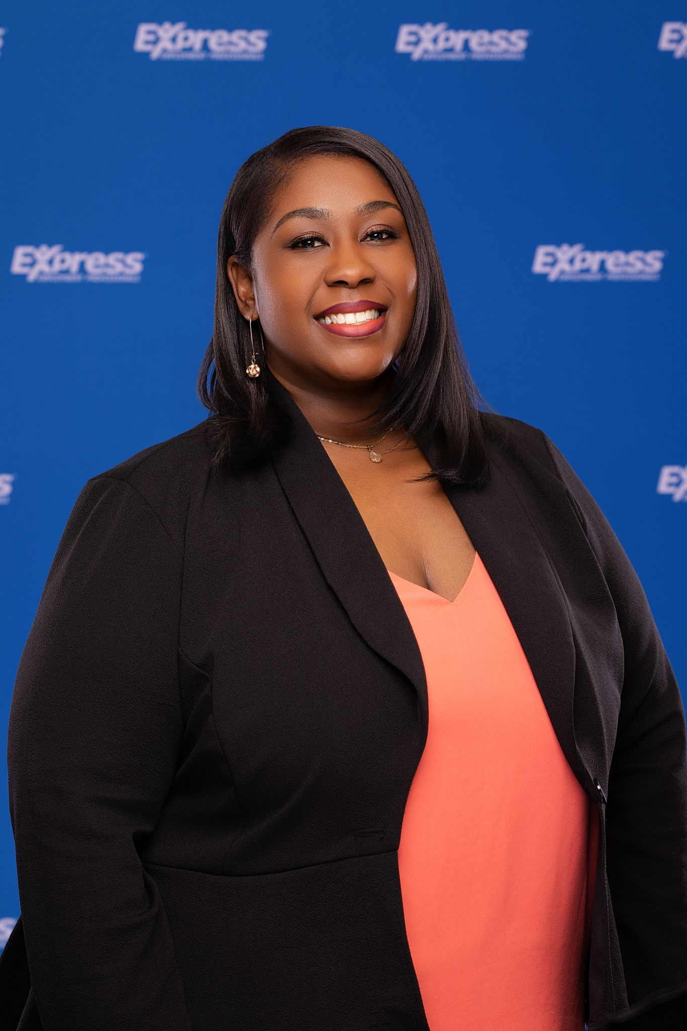 Professional woman smiling in black blazer before Express Employment backdrop.