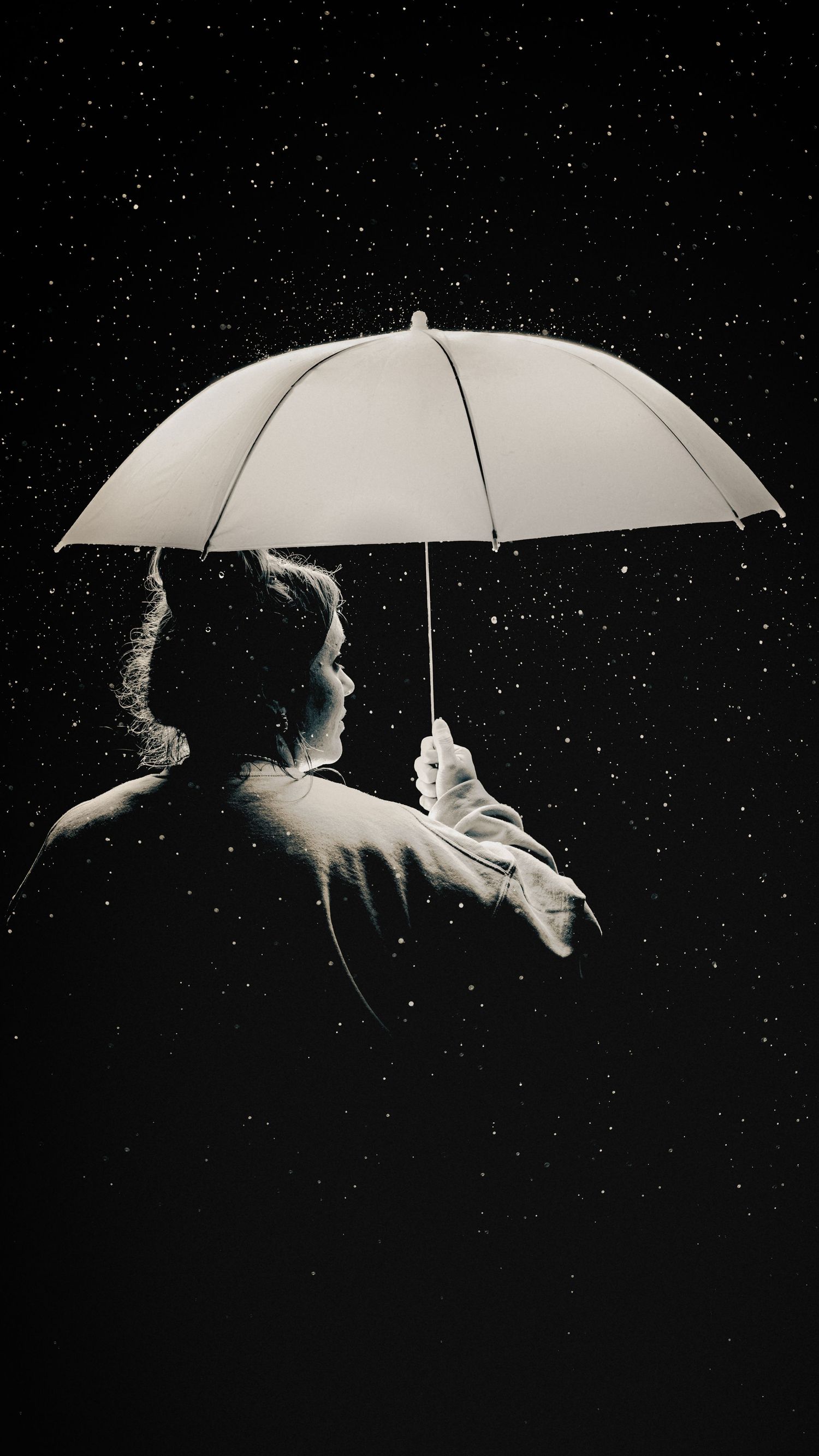 Black and white silhouette of person holding white umbrella under starry night sky.