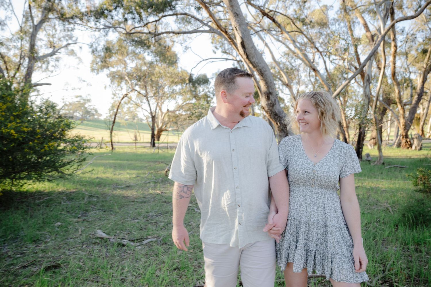 Couple in light summer attire walking together through a scenic countryside landscape with gum trees.