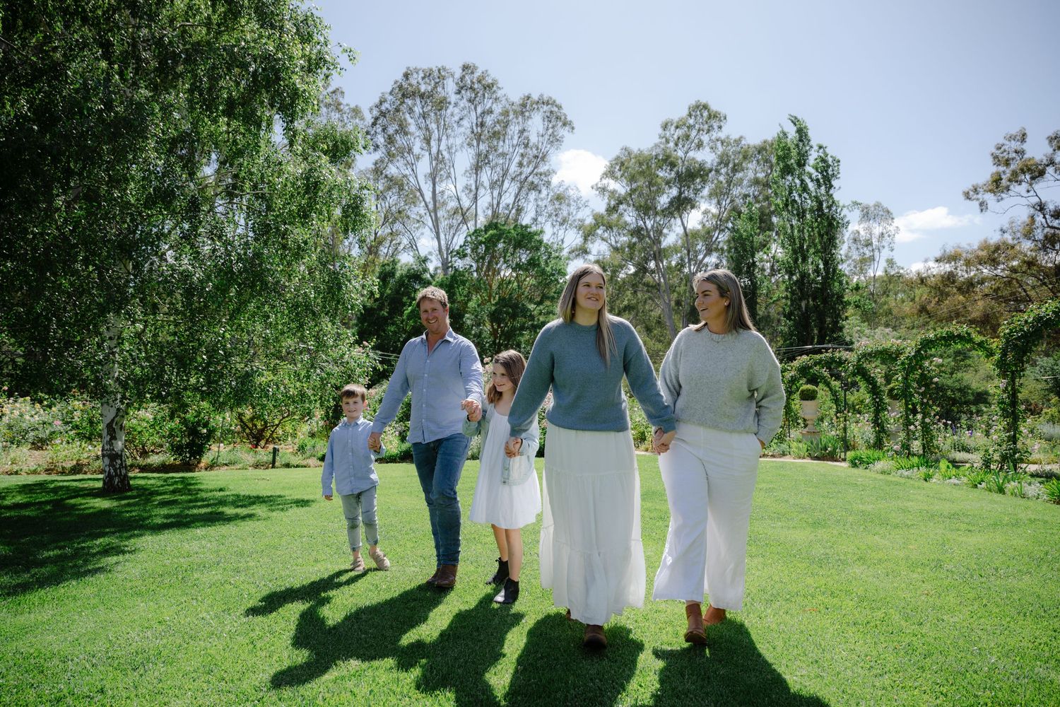 Group walking together on grassy path through lush green park on sunny summer day.