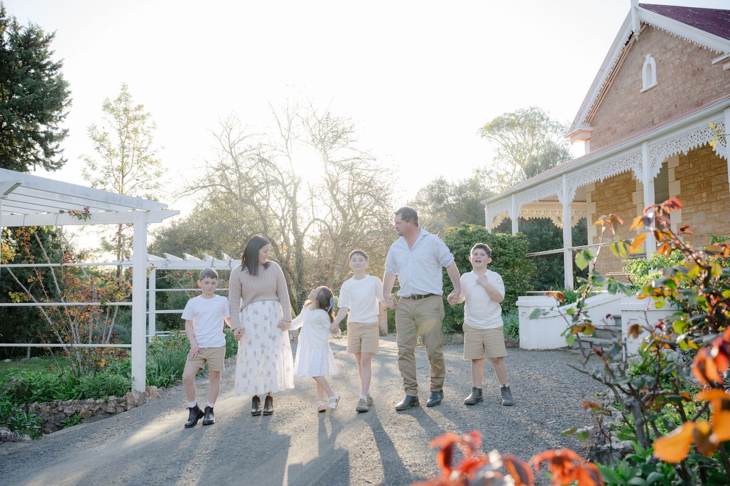 A group walks together down a garden path at sunset with a charming brick house and colorful flowers in the background.
