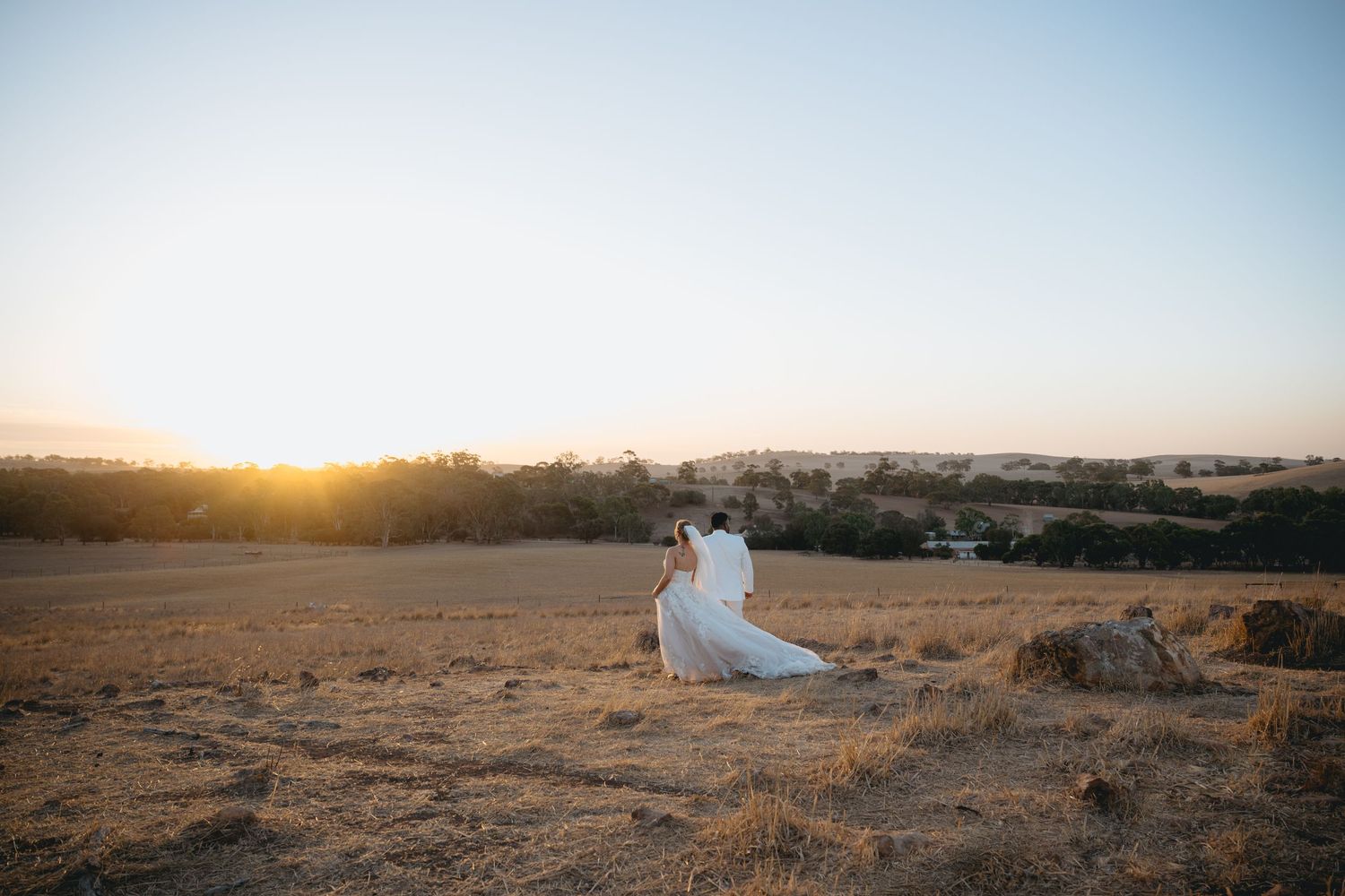 Romantic sunset wedding photos captured in a golden field with soft lighting and dramatic sky.