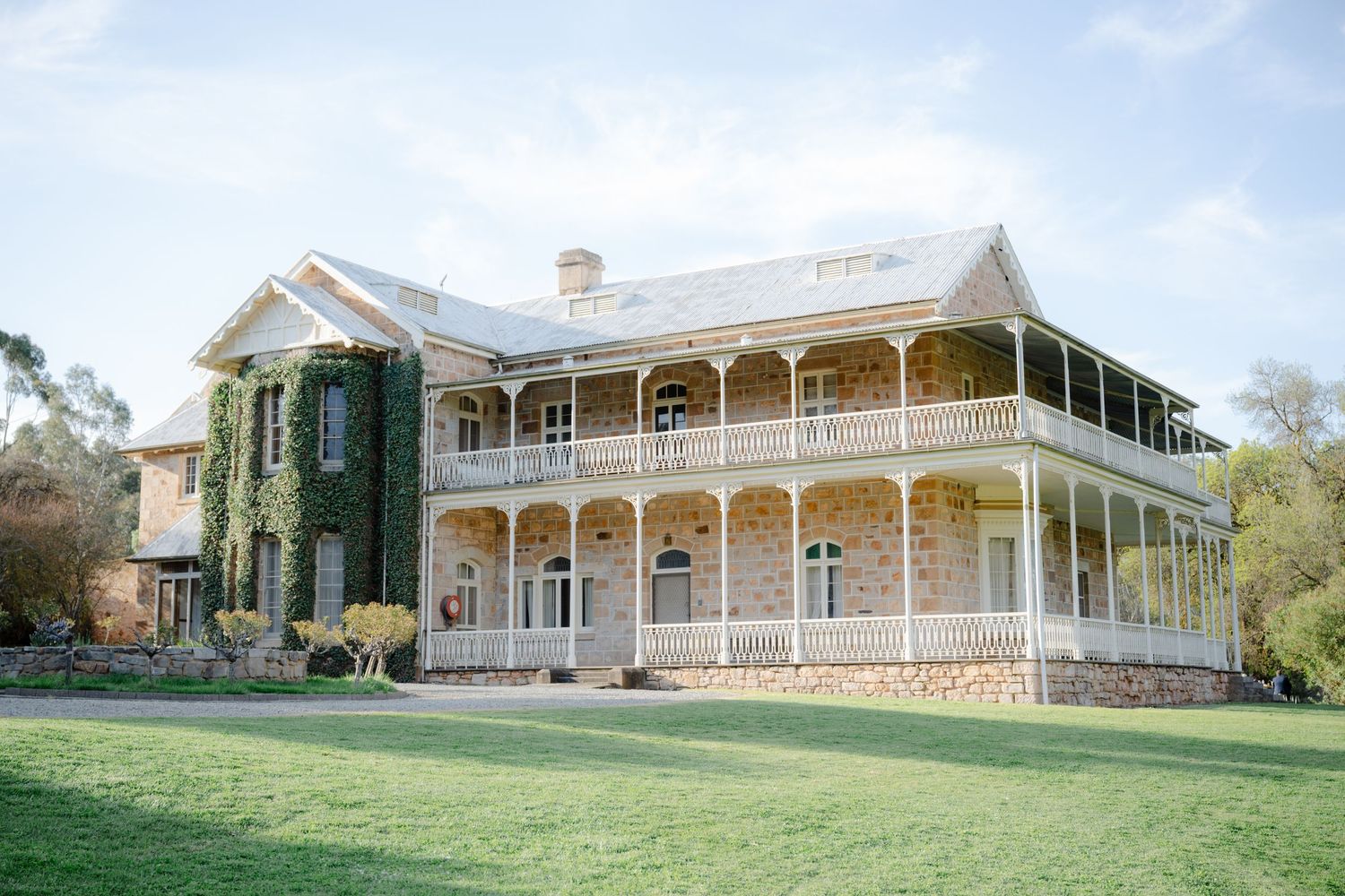 A panoramic view of a historic white colonial mansion with wraparound verandas set on a grassy hillside estate.