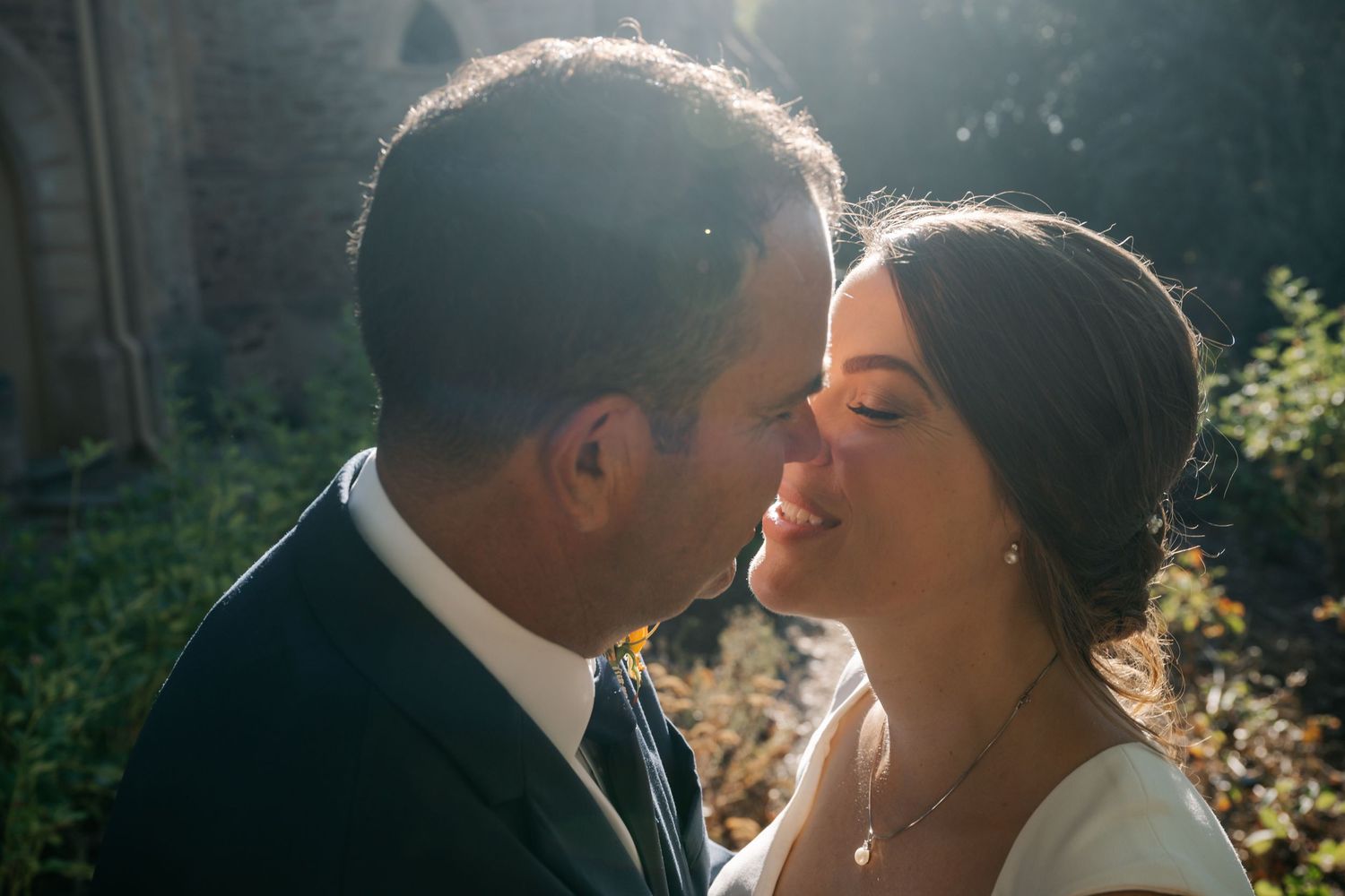 A romantic moment captured between newlyweds in sunlit garden setting during their wedding day.