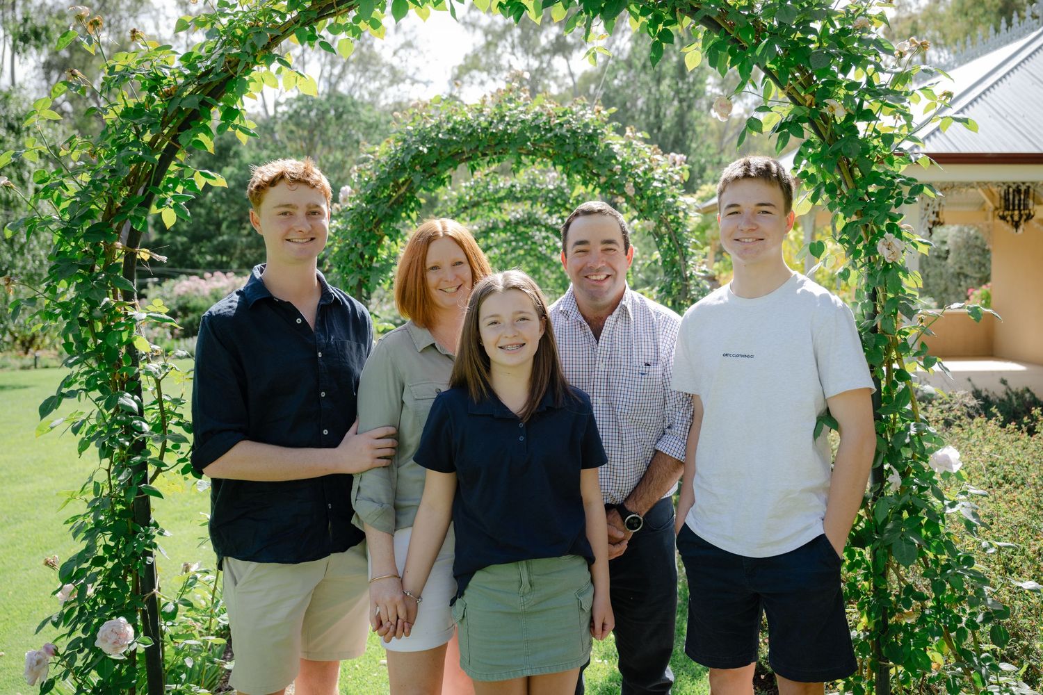 Family members pose together under a lush green garden archway during an outdoor gathering.