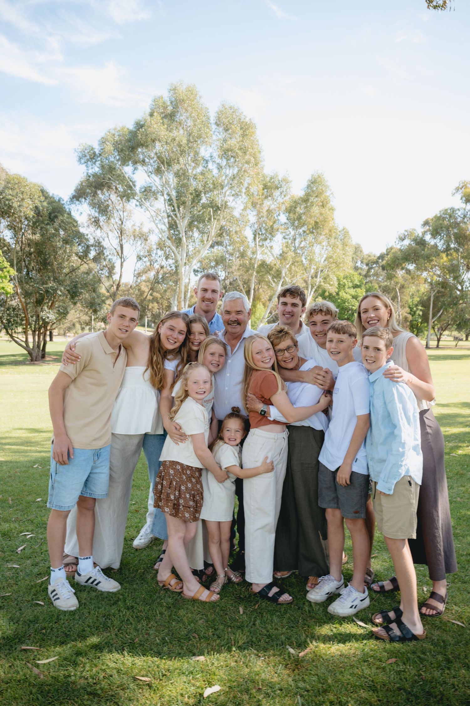 A group of people stand together outdoors on green grass with eucalyptus trees in the background.