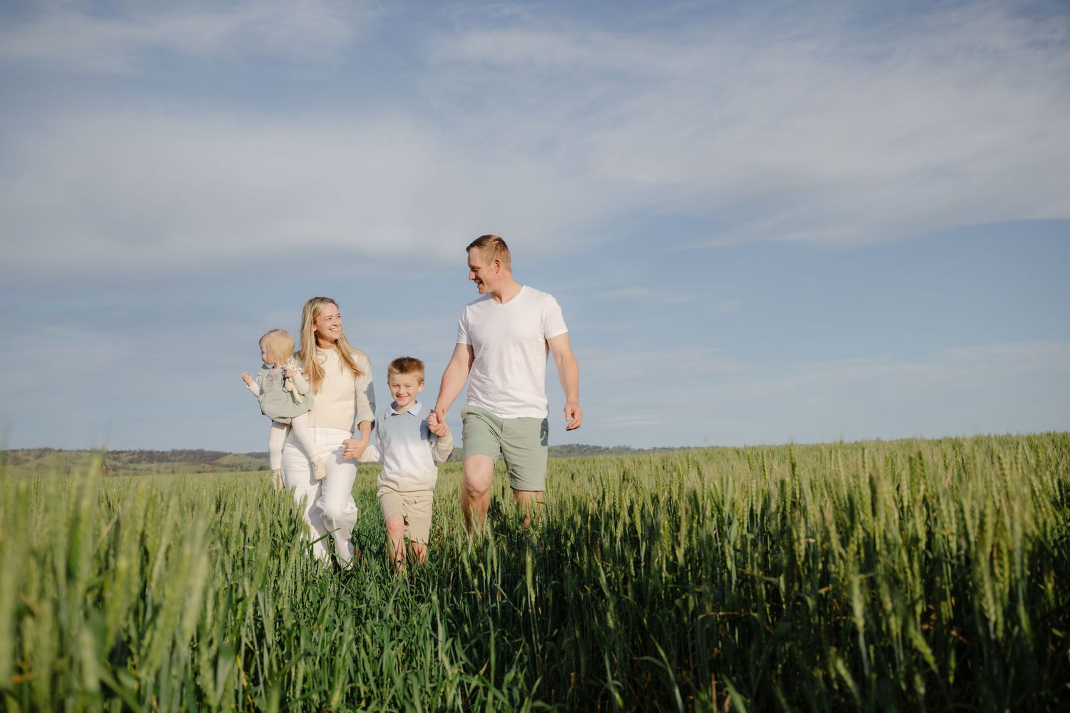 Family walking together through a lush green cornfield on a sunny summer day with blue sky overhead.