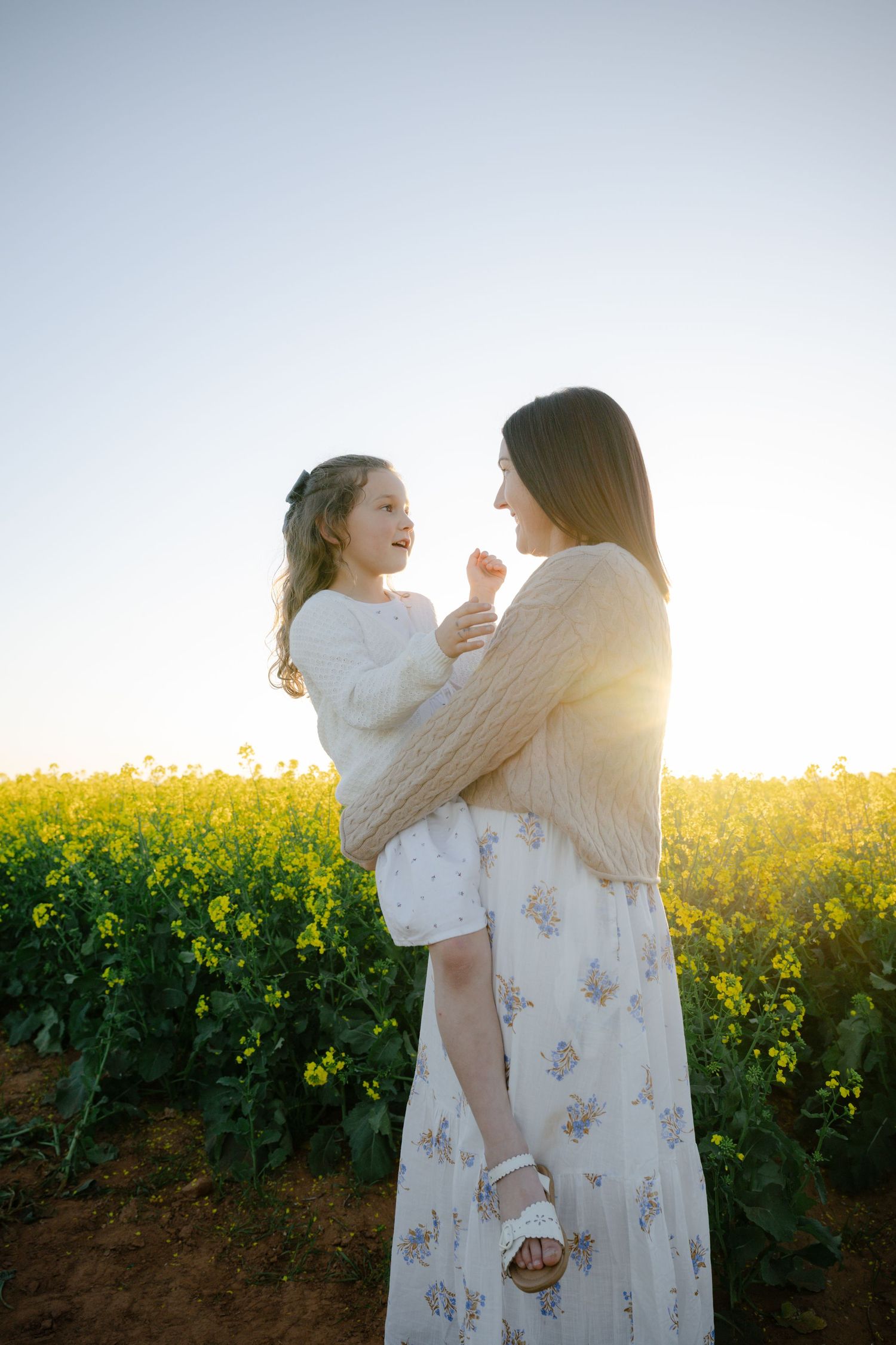 Two people sharing joyful moments in a blooming yellow canola field at golden hour.